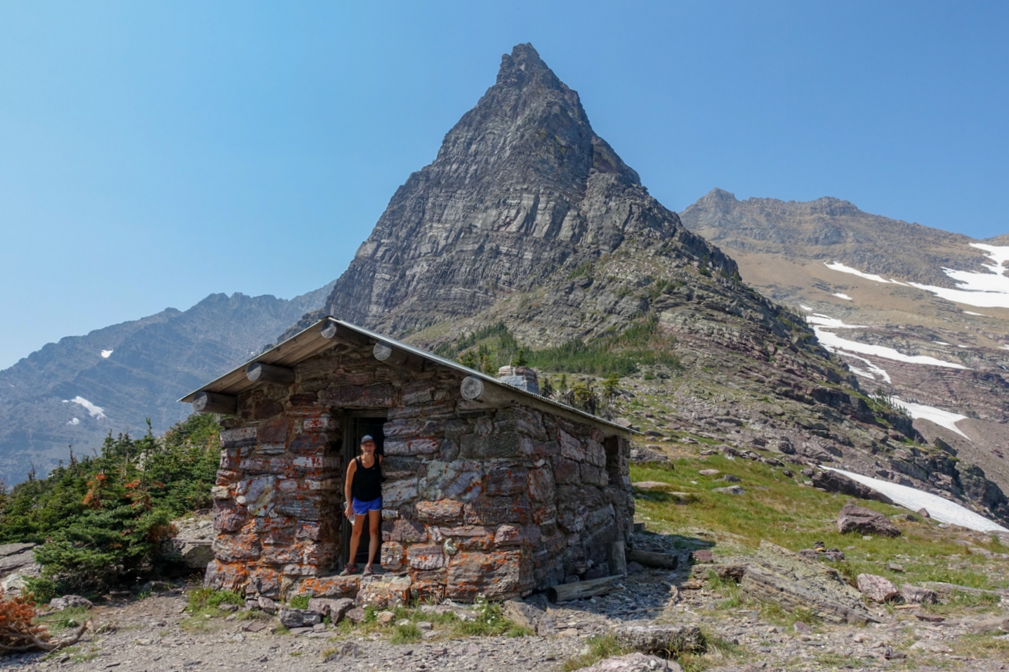 sperry chalet, a stone and wooden alpine hut with peaks and snow behind it.