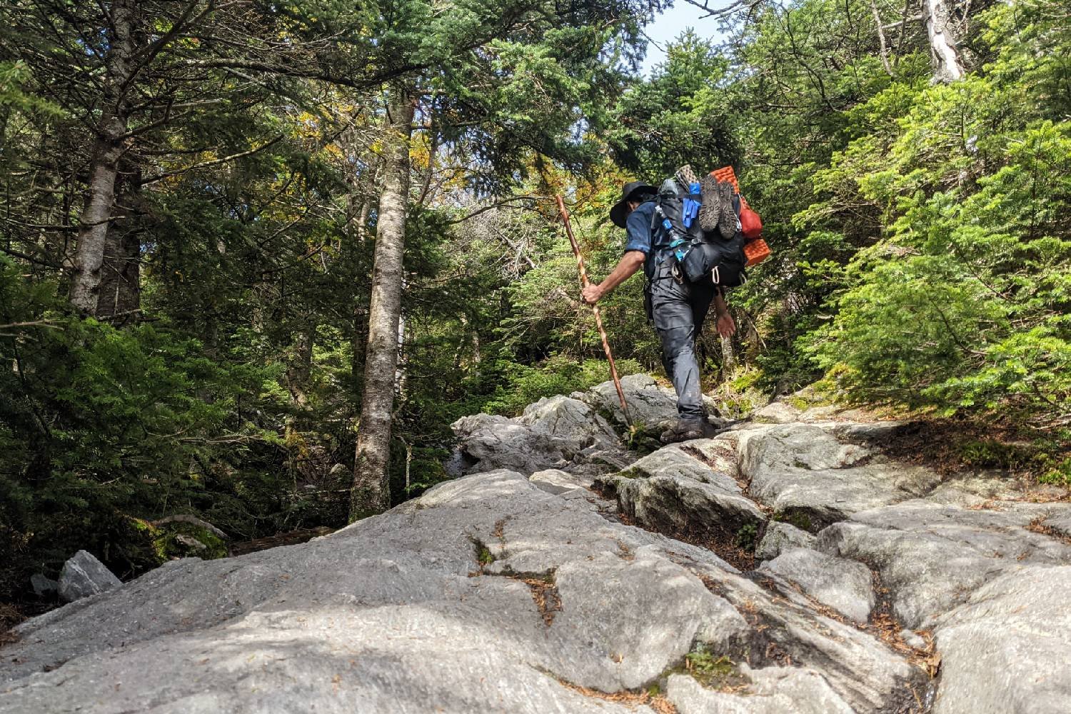 a backpacker on the long trail walking on rocky slabs with a hand carved wooden hiking stick