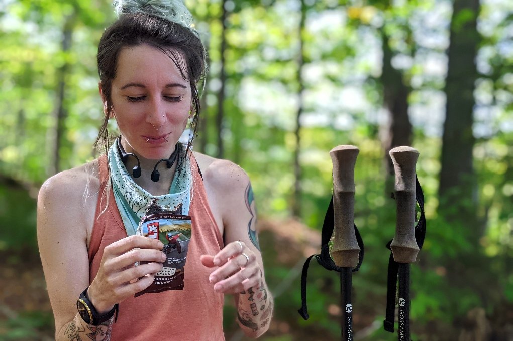 backpacker with headphones around her neck eating a clif bar on vermont's long trail.