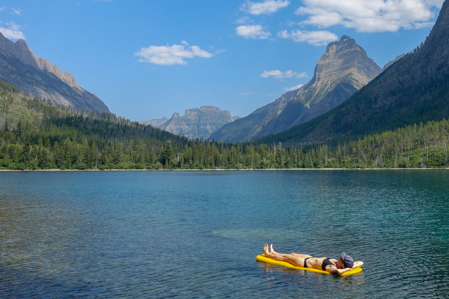 backpacker floating on their sleeping pad on a lake in glacier national park