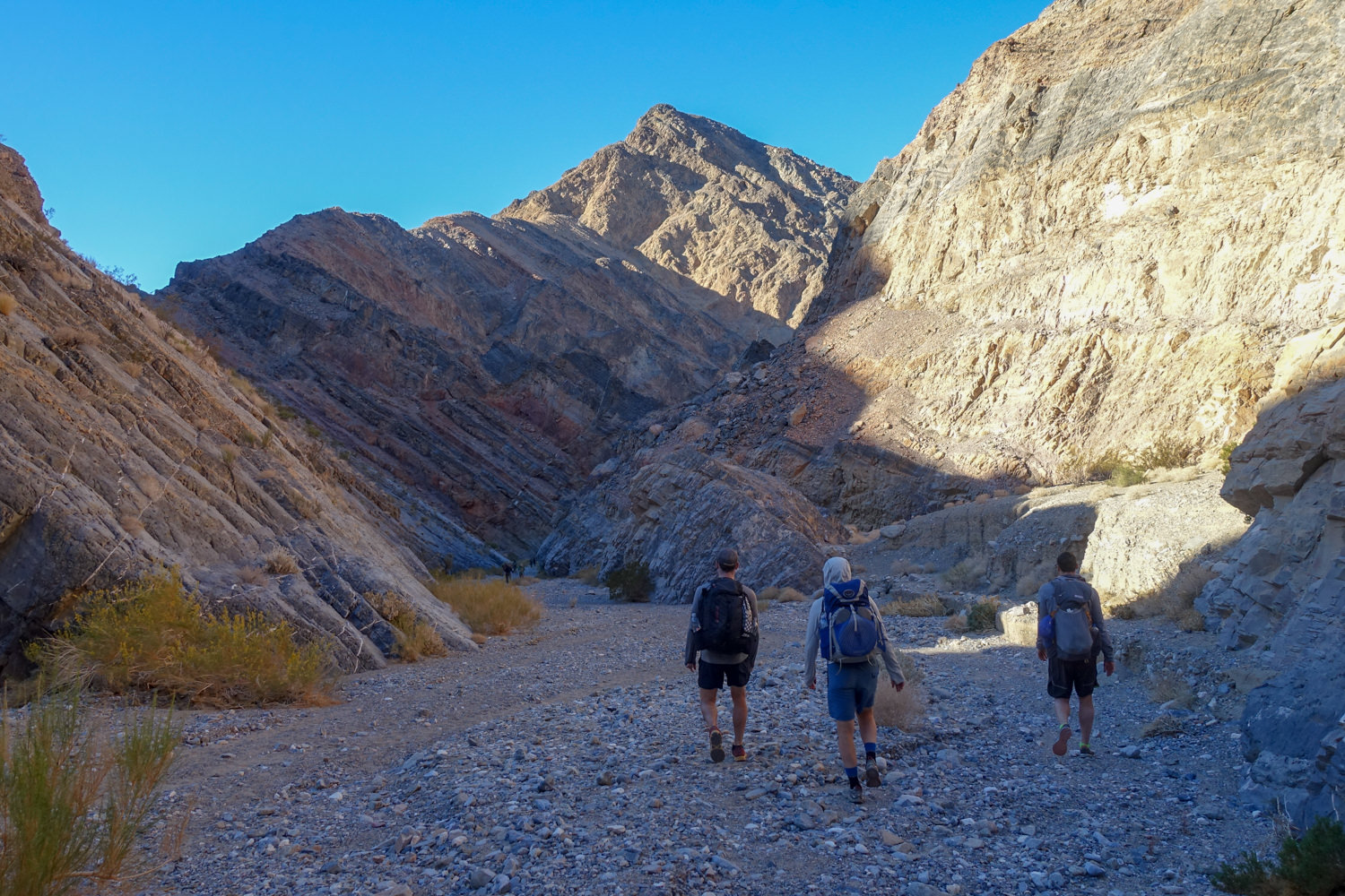 three backpackers walking into a canyon in death valley