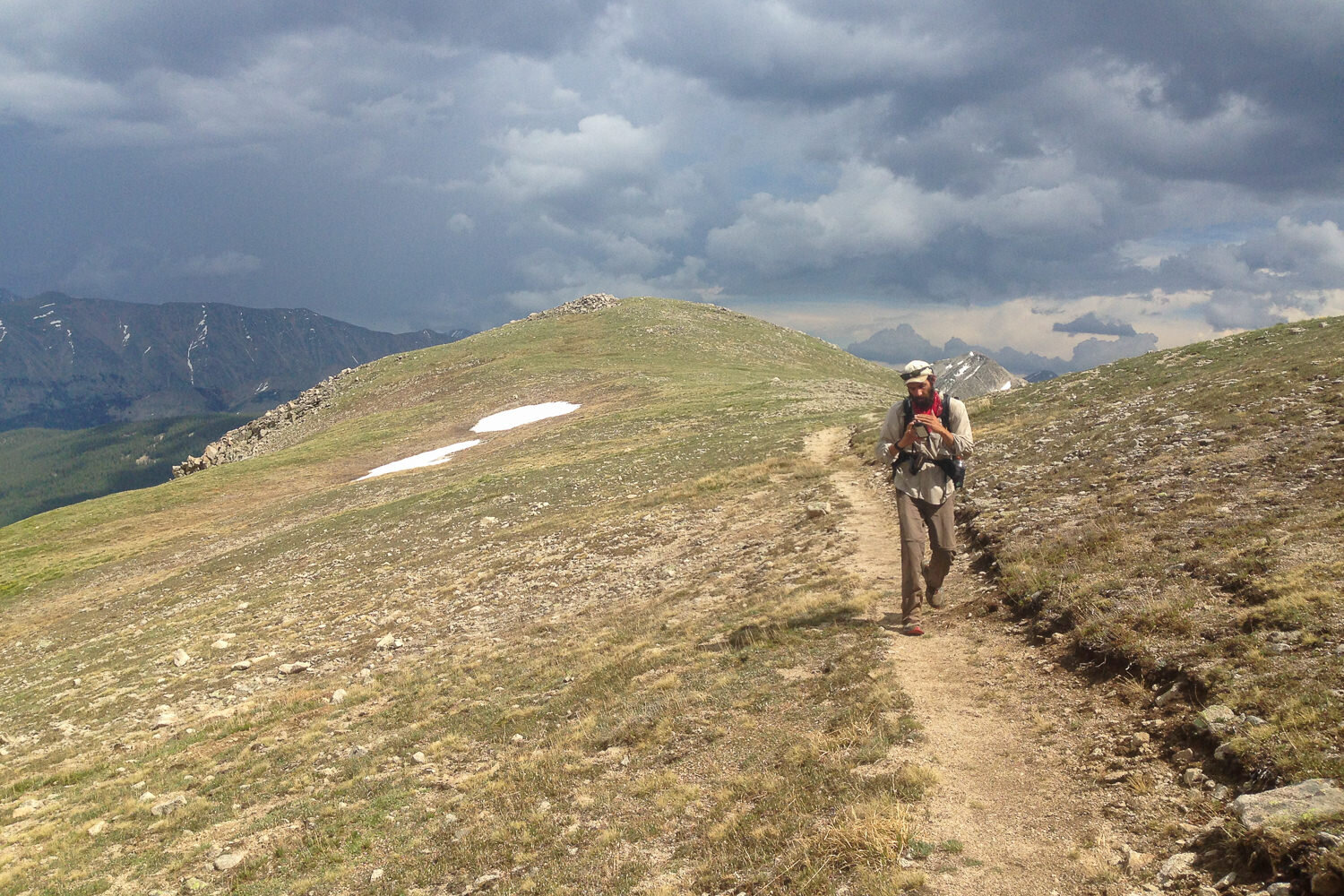 CDT thru-hiker walking away from storm clouds.