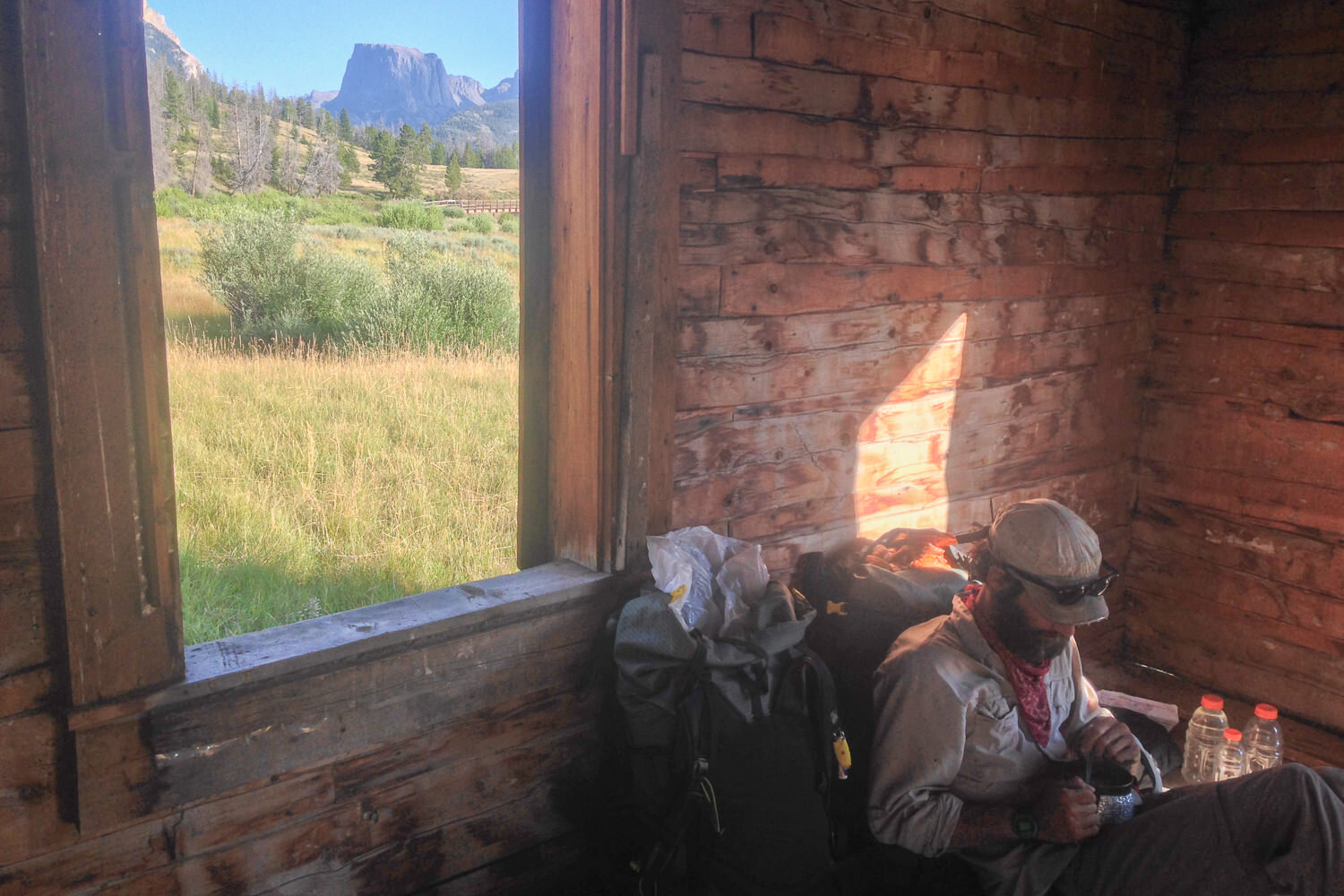 CDT thru-hiker sitting next to a window in a backcountry cabin