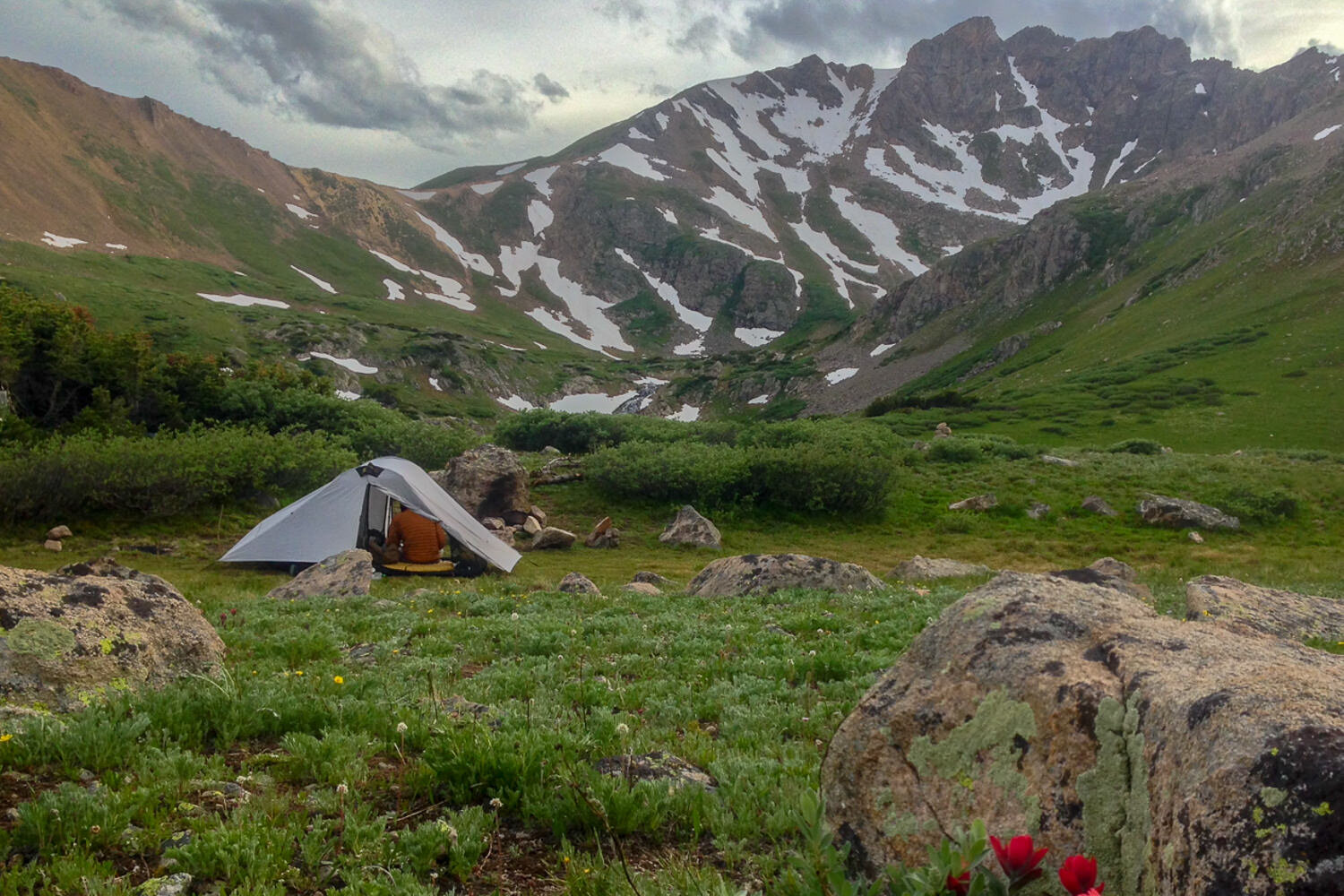 tent set up on the CDT in a green valley with mountains behind