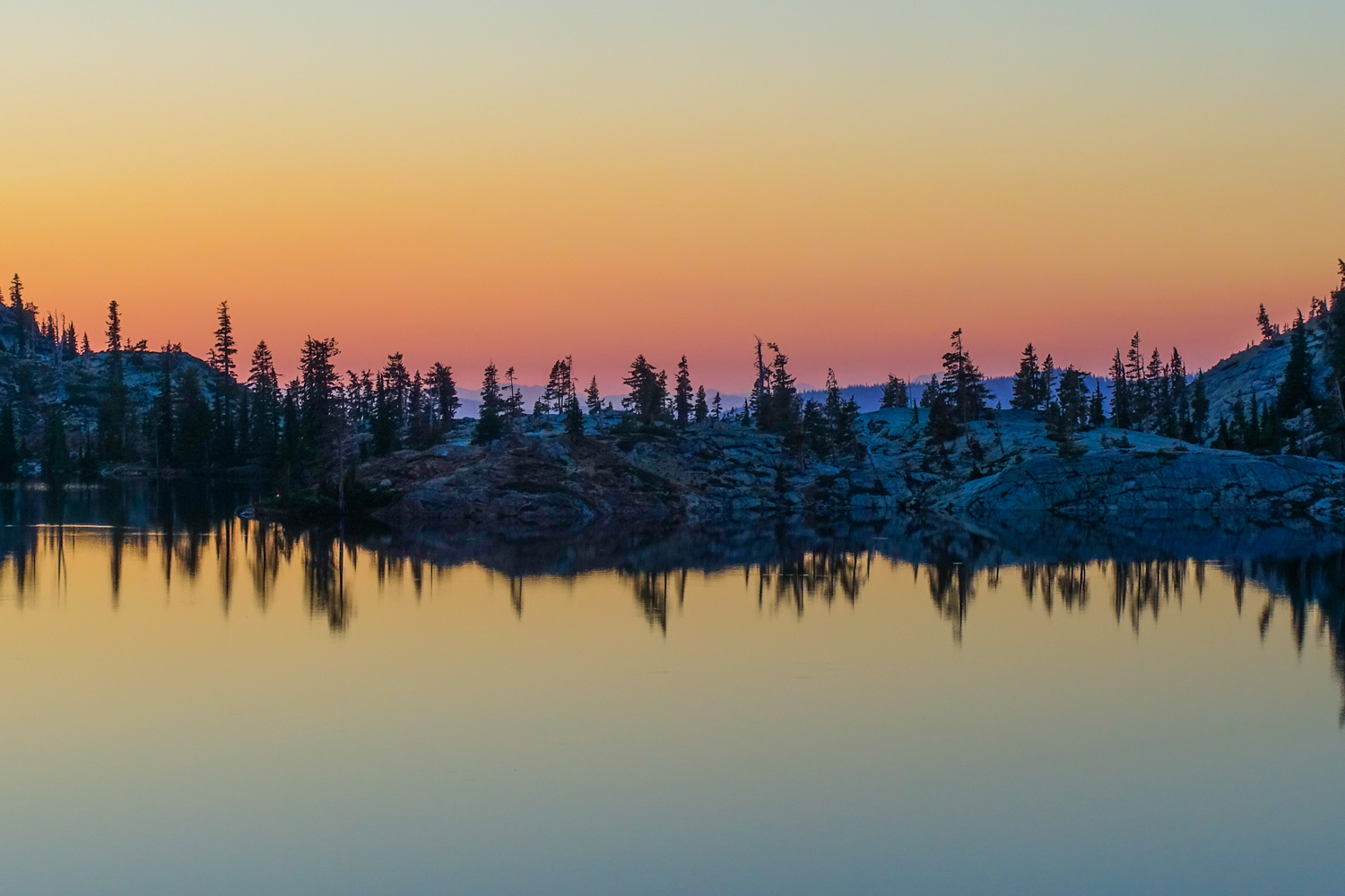 orange, yellow and pink sunset on an alpine lake in the trinity alps wilderness with the trees and sunset reflected on the lake