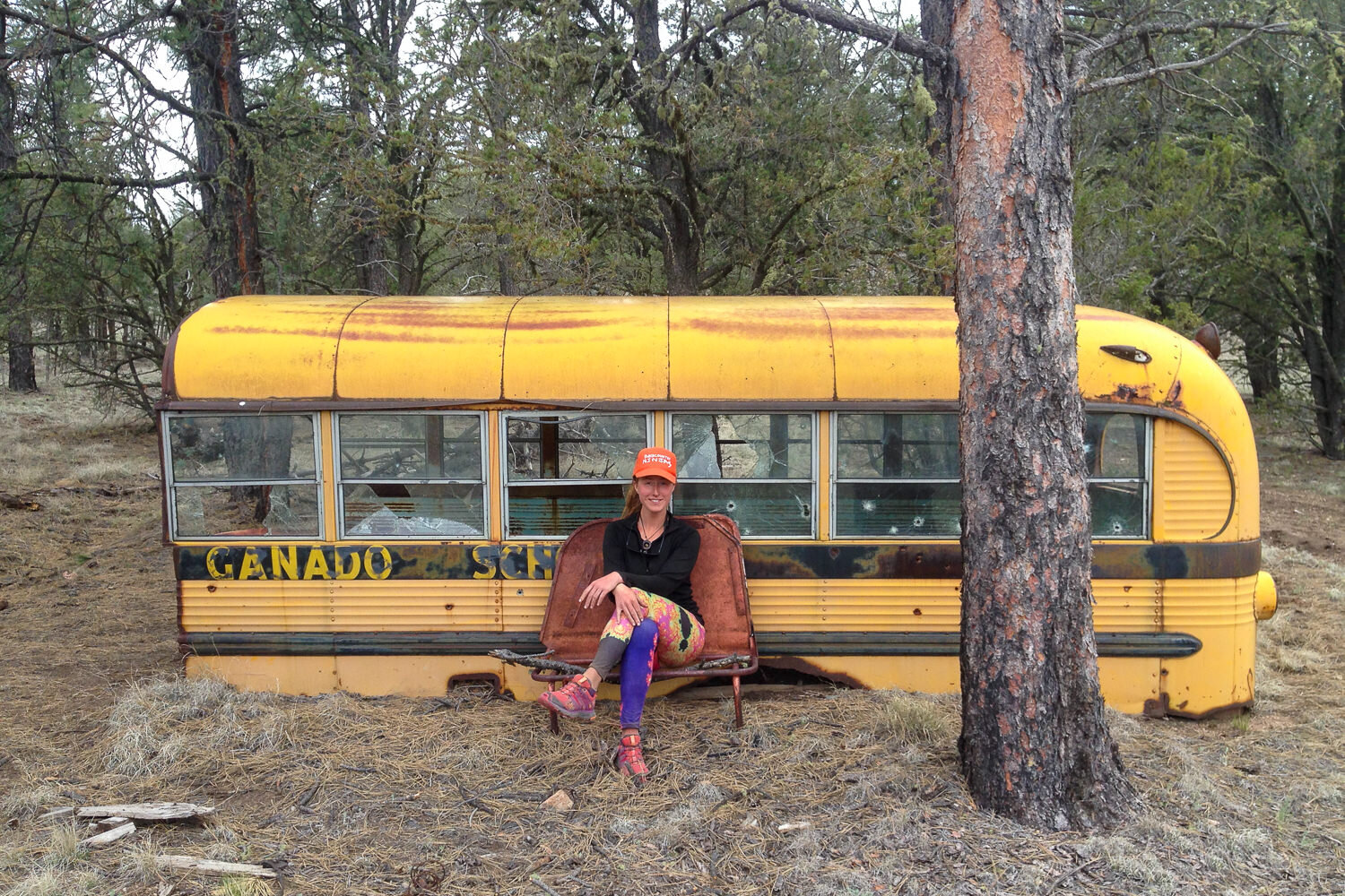 rusting abandoned school bus in the forest on the CDT with a hiker posing in front of it