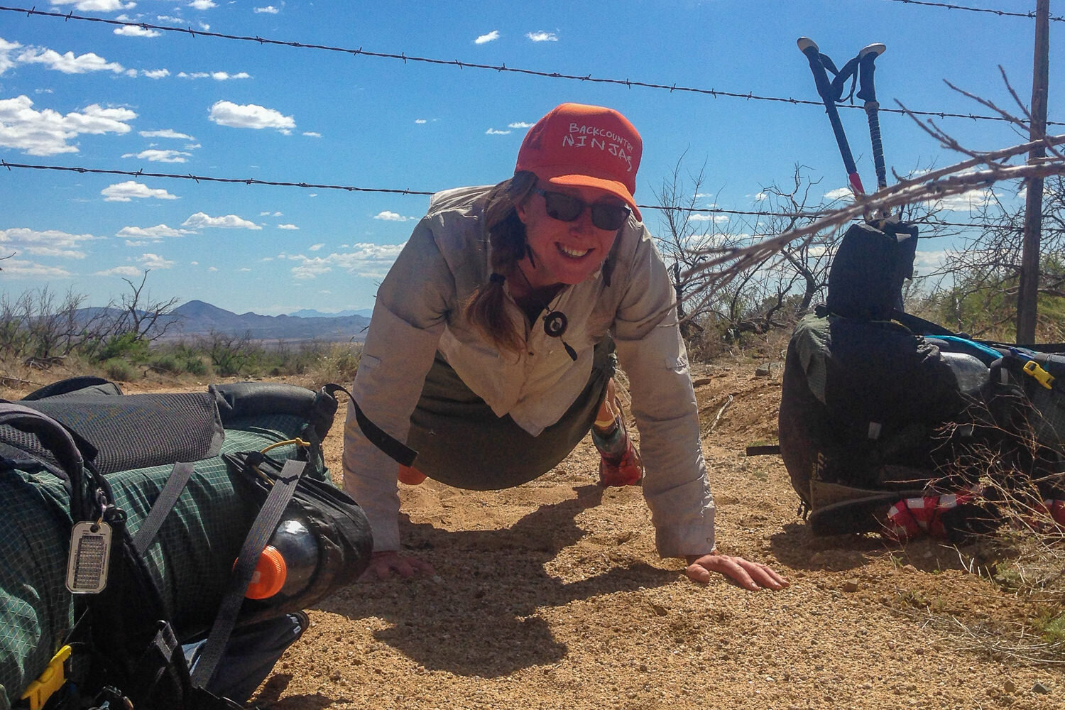 CDT thru-hiker crawling under a cattle fence.