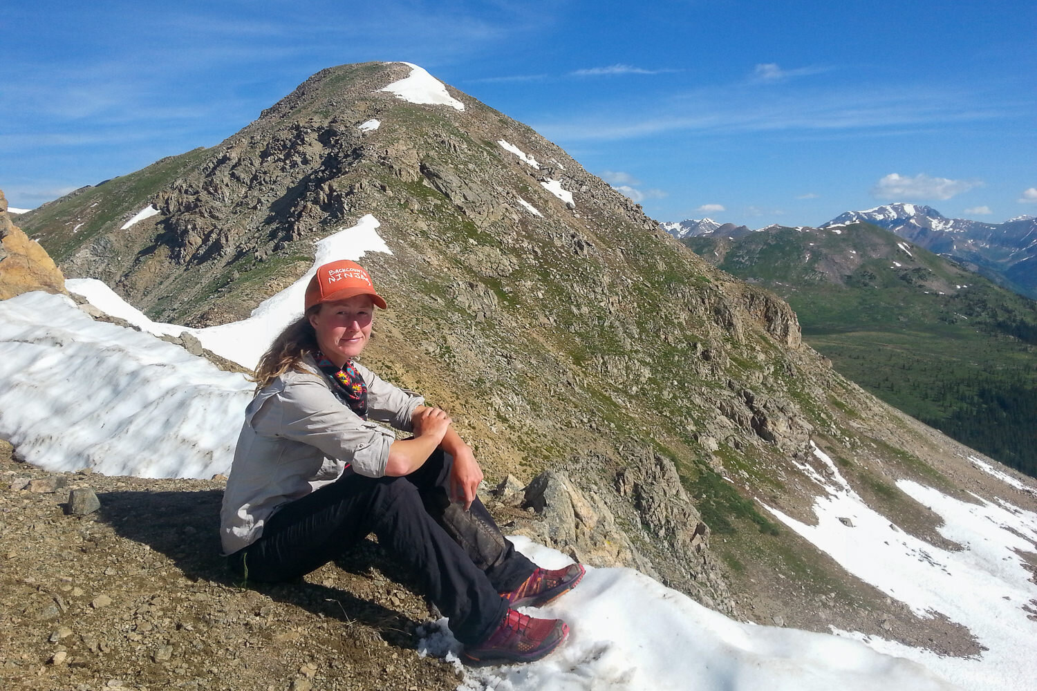 Backpacker on the CDT taking a break on a mountain ridge with snow still holding onto the mountain.