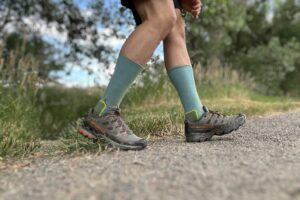 A hiker from the knees down walks on a trail in a forest setting.