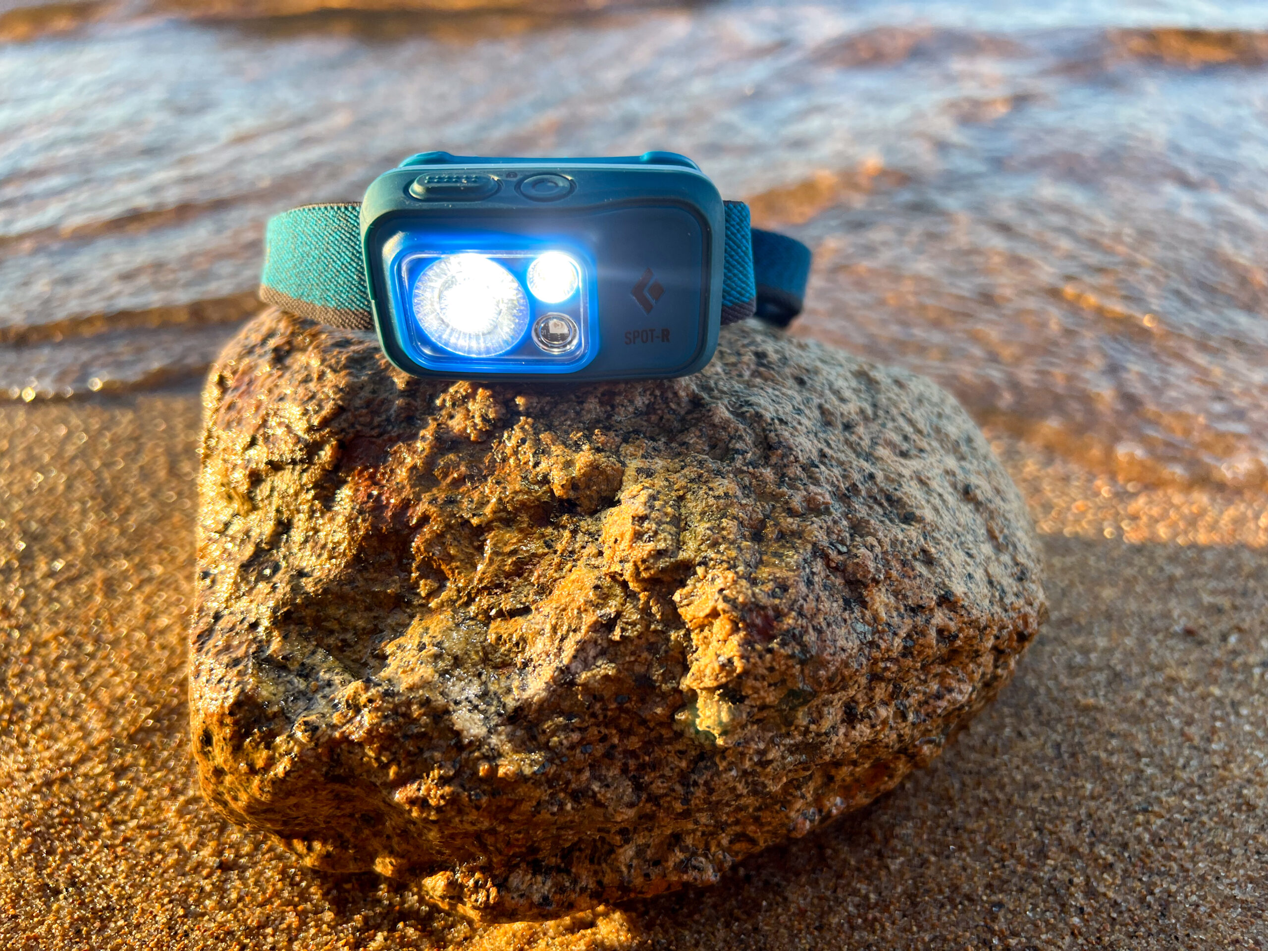 The image shows a Black Diamond Spot 400 - R sitting on a rock next to water.