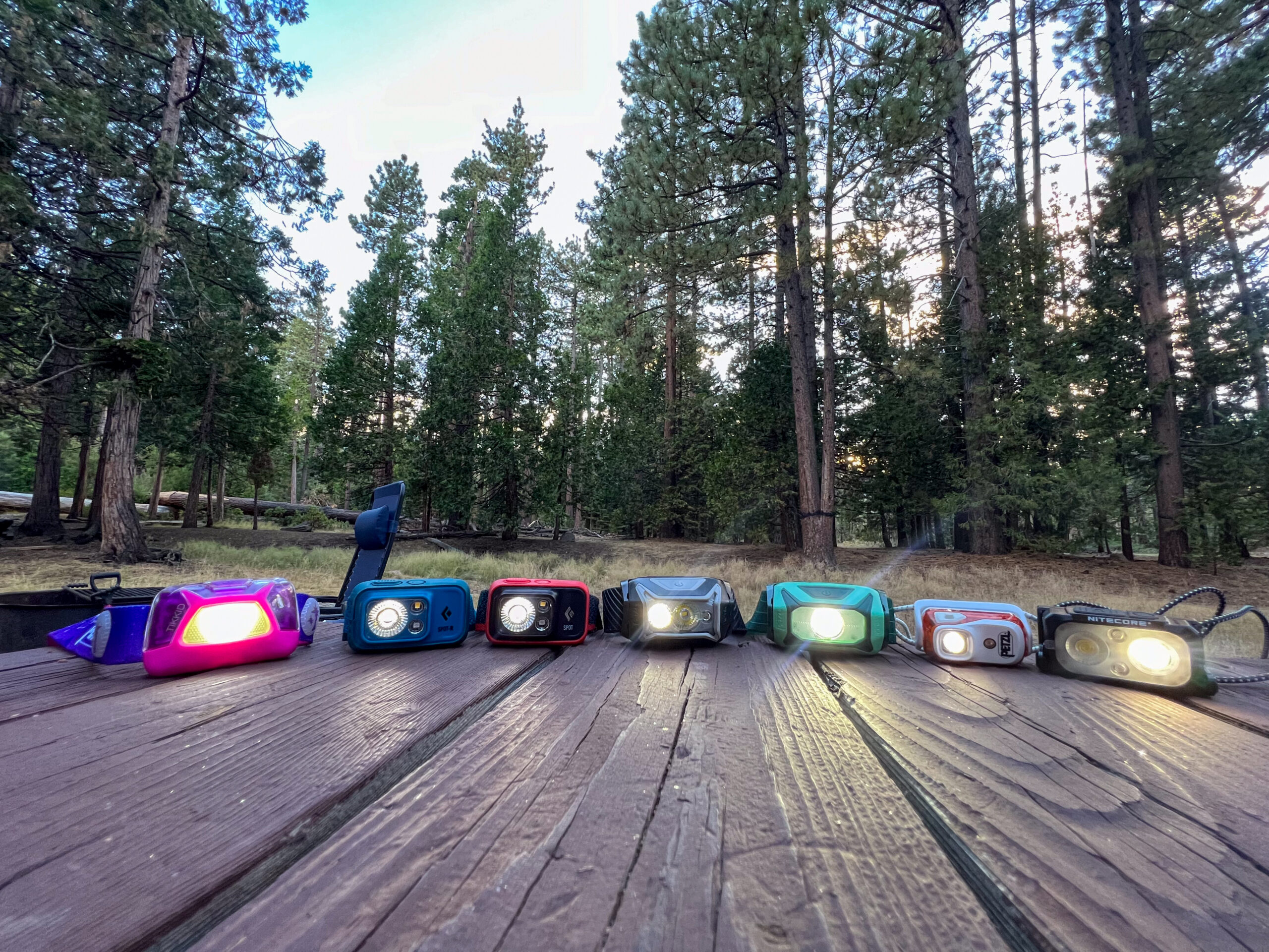 The image shows a semi-circle of headlamps in a forest setting.