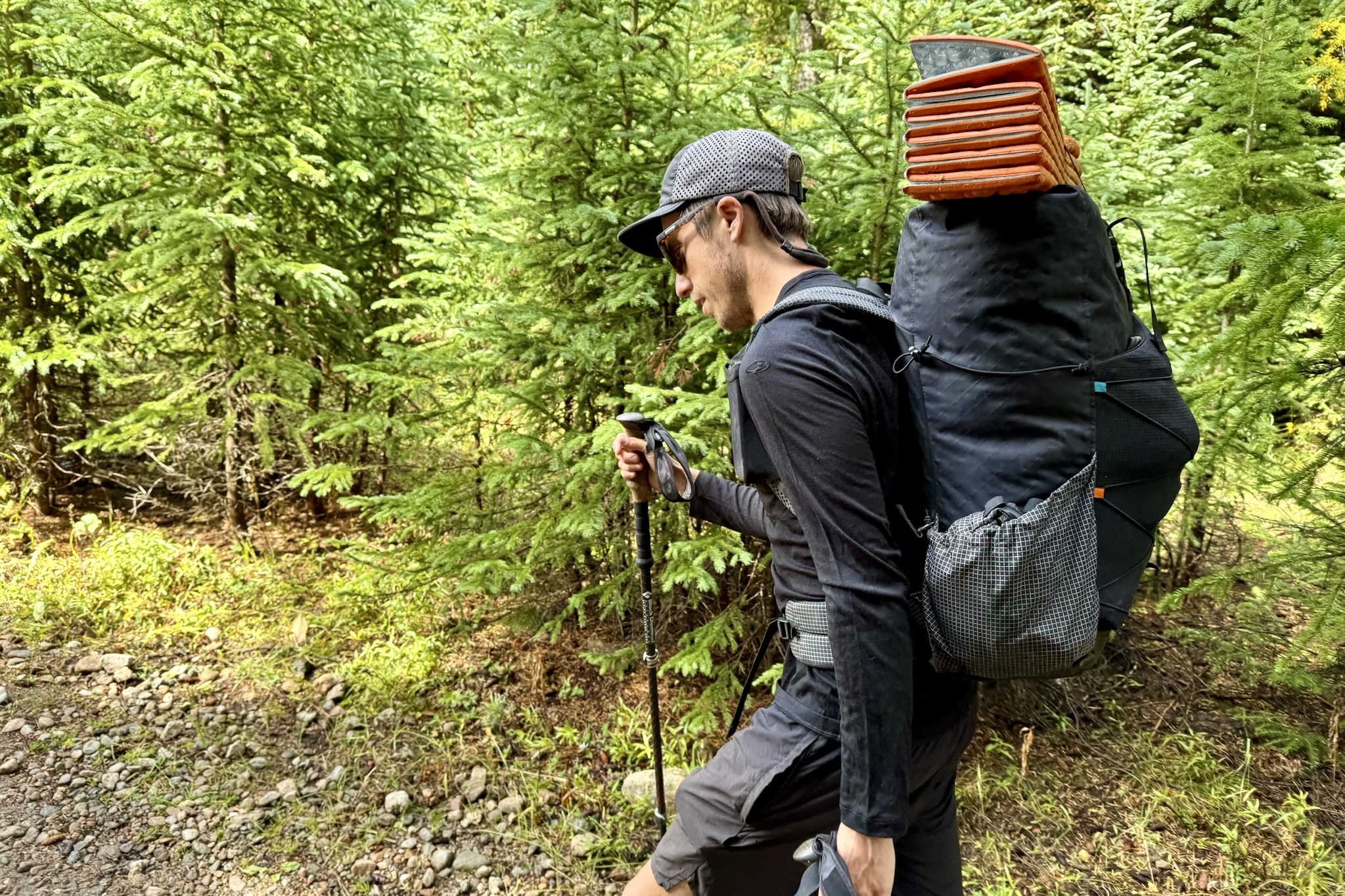 A hiker walks through the woods with a pack while wearing the Icebreaker Oasis 200 base layer. Trees are in the background.