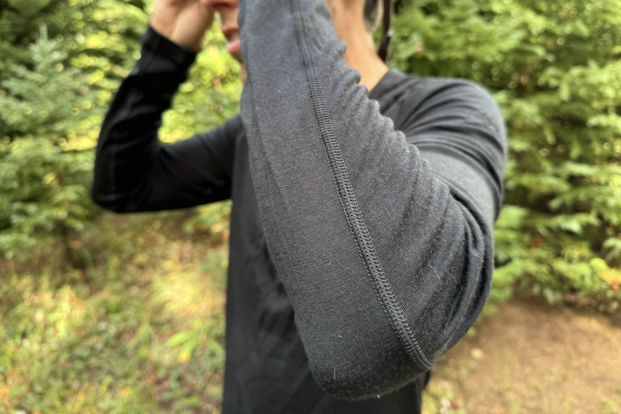 A hiker bends his elbows, showing the seams of the Icebreaker Oasis 200 base layer. Trees are in the background.