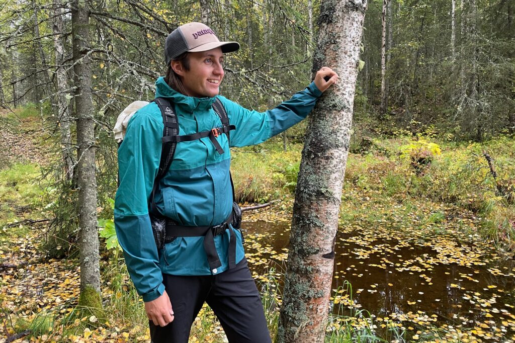 A man leans against a tree in a forest setting.