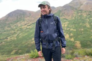 A man smiles while wearing a rain jacket in the alpine.
