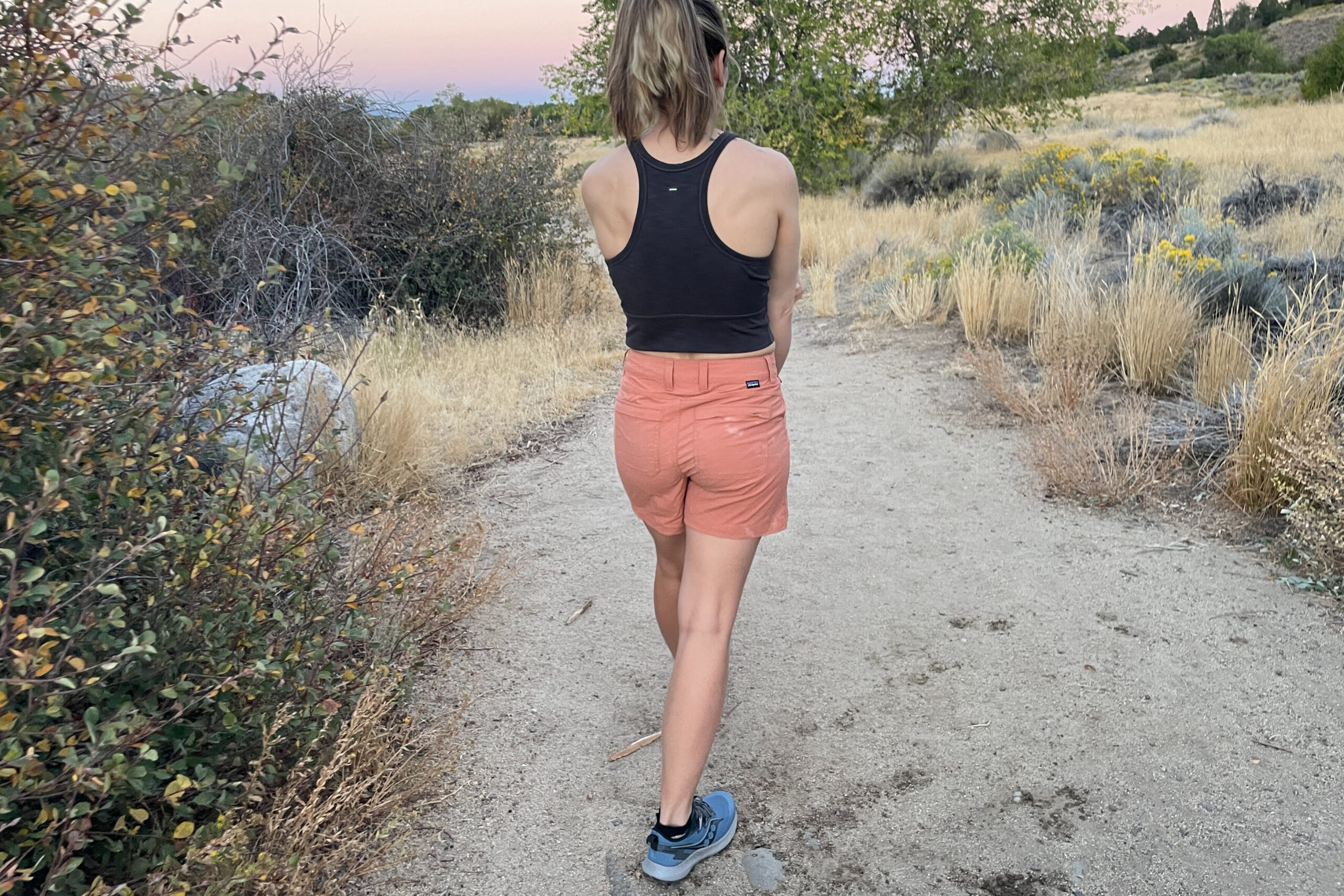 a person walking away from the camera on a sandy trail in sunset