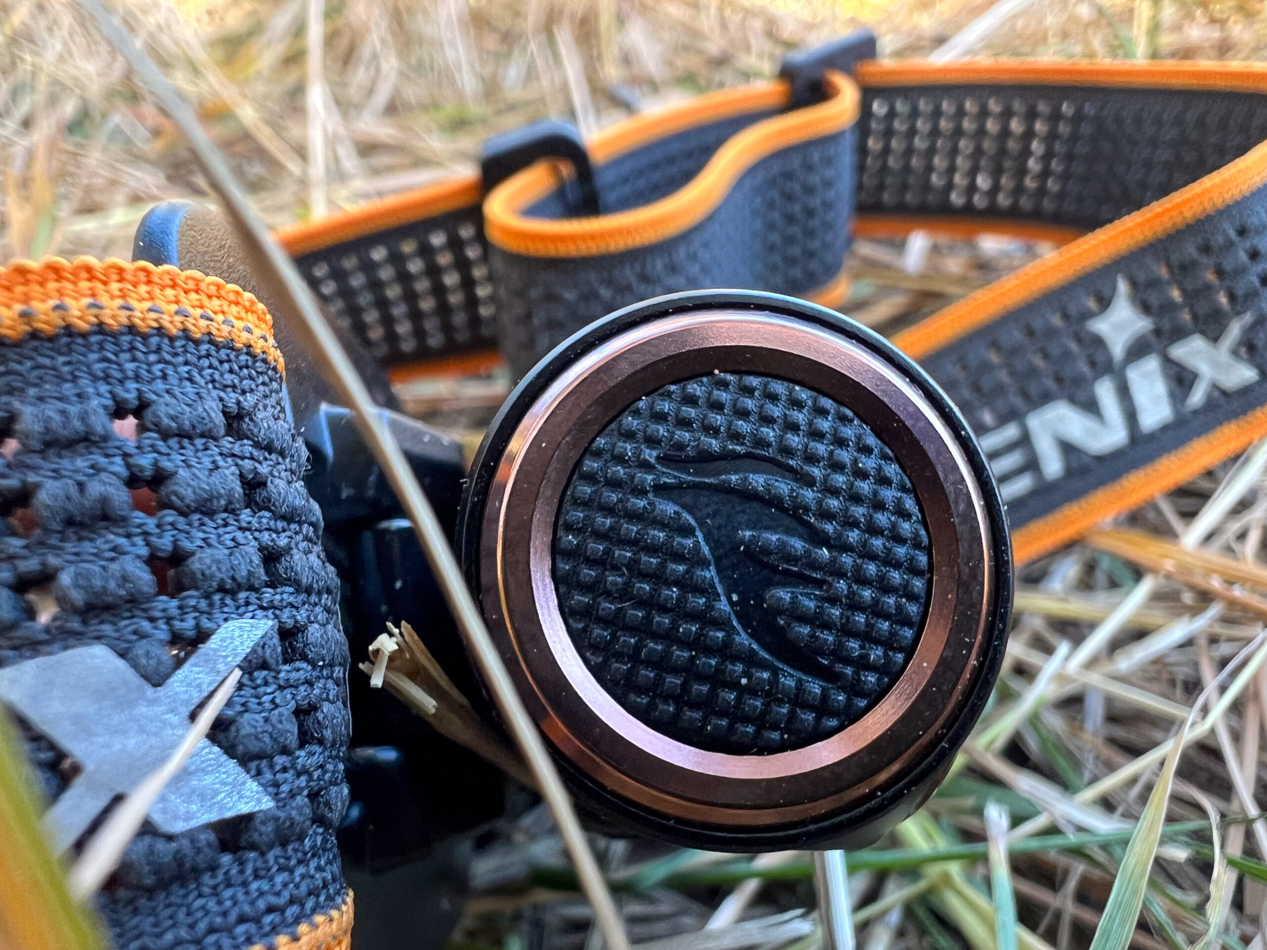 The image shows a close-up of the power button on the Fenix HM50R V2.0 headlamp. The button is circular and surrounded by a metal ring with a copper-colored finish.