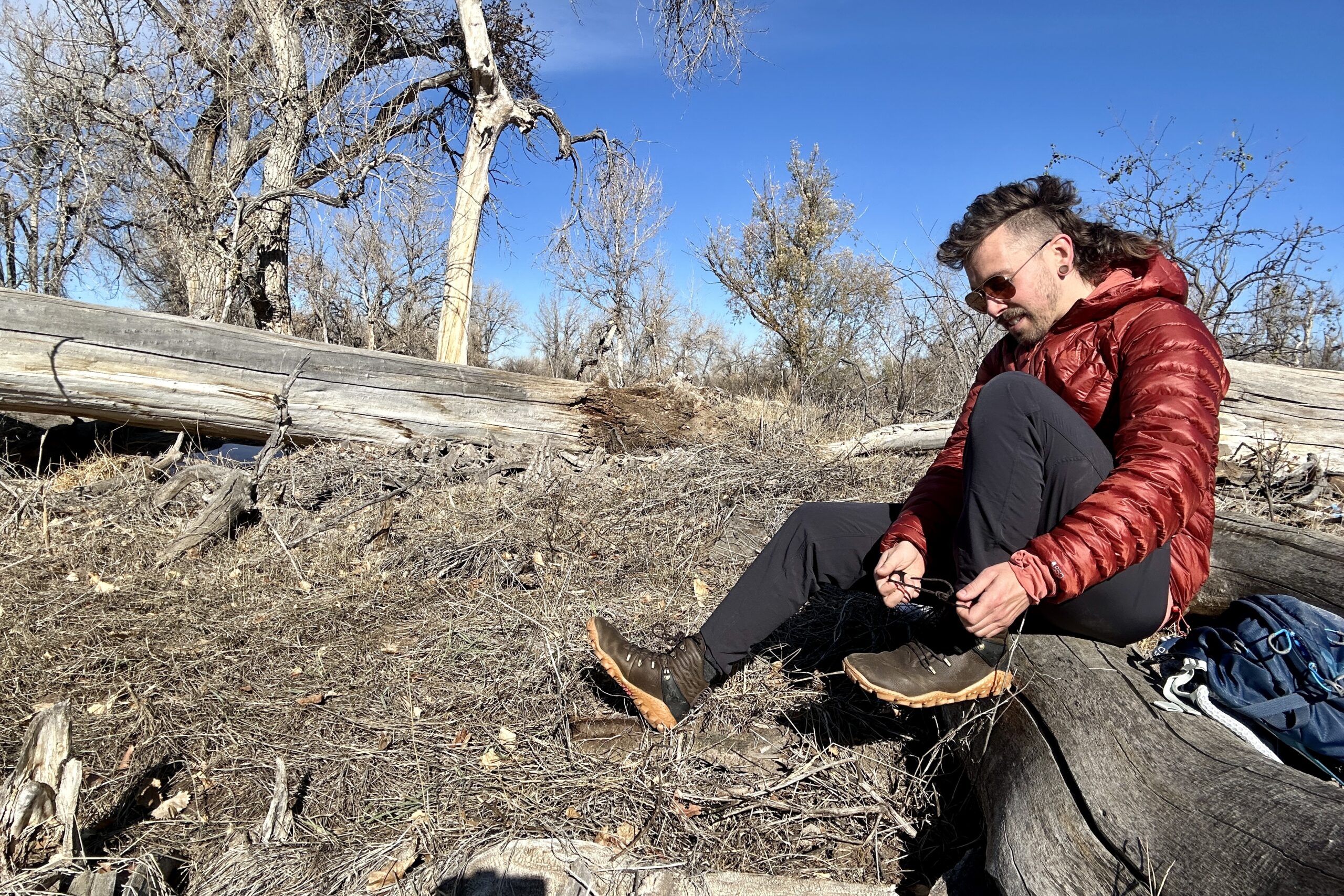 A man ties his shoes while sitting on a log in a wilderness area.