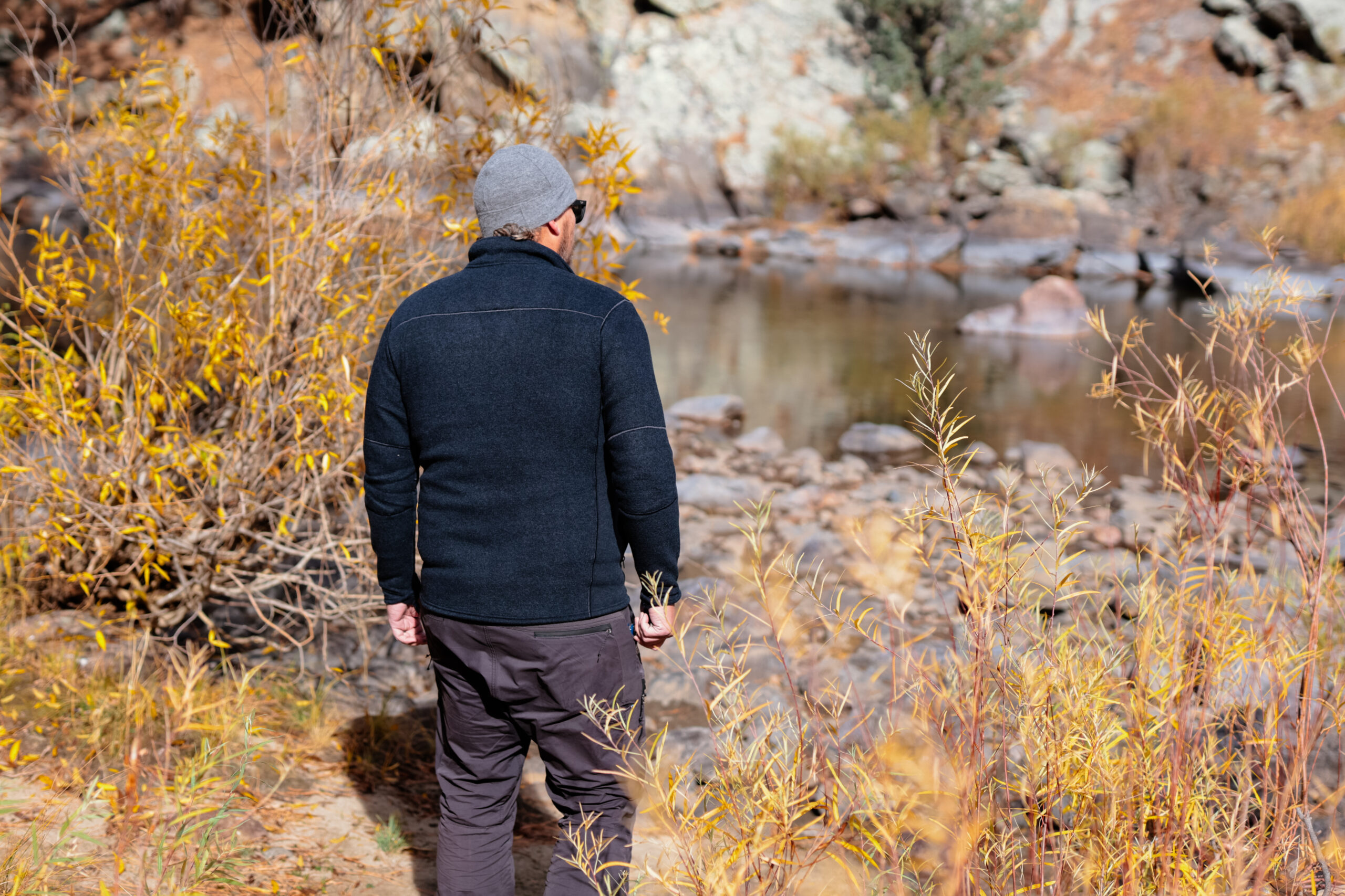 A man walks by a river in fall leaves.