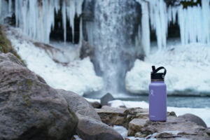 The Hydro Flask Wide Mouth sits on a rock with a partially frozen waterfall in the background.
