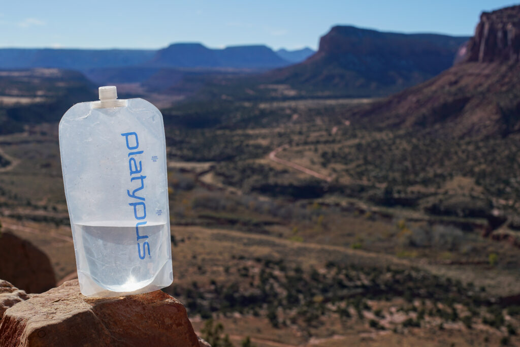 A half-filled Platypus Platy Bottle sits on a rock with mesas in the background.