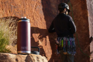 The YETI Rambler sits on a rock with a climber standing in the background.