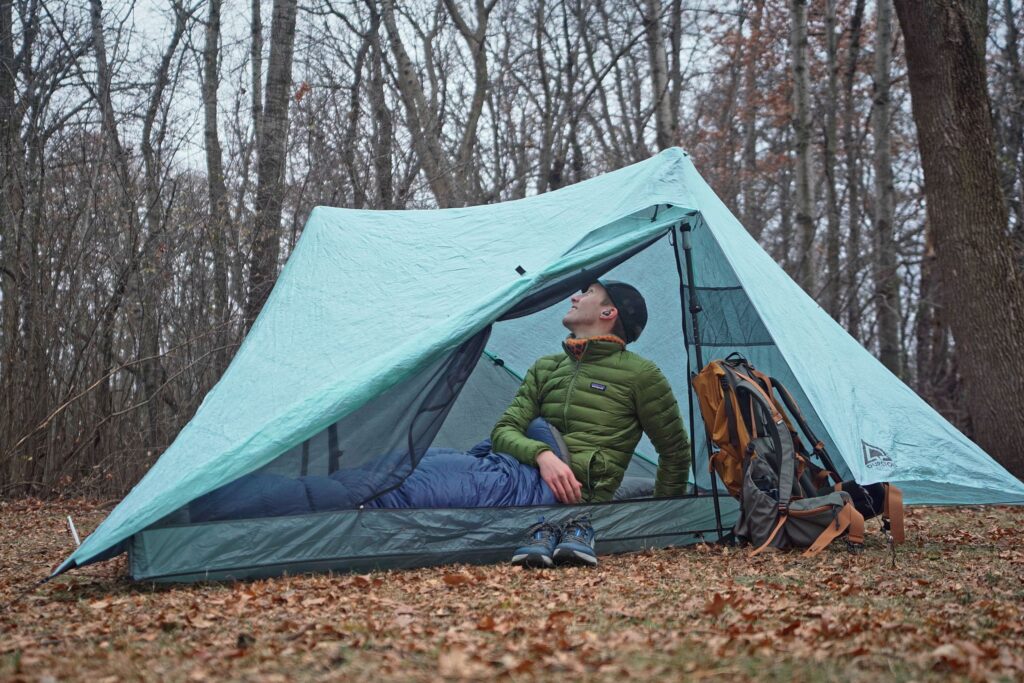 a man in a green coat sits in a two person tent