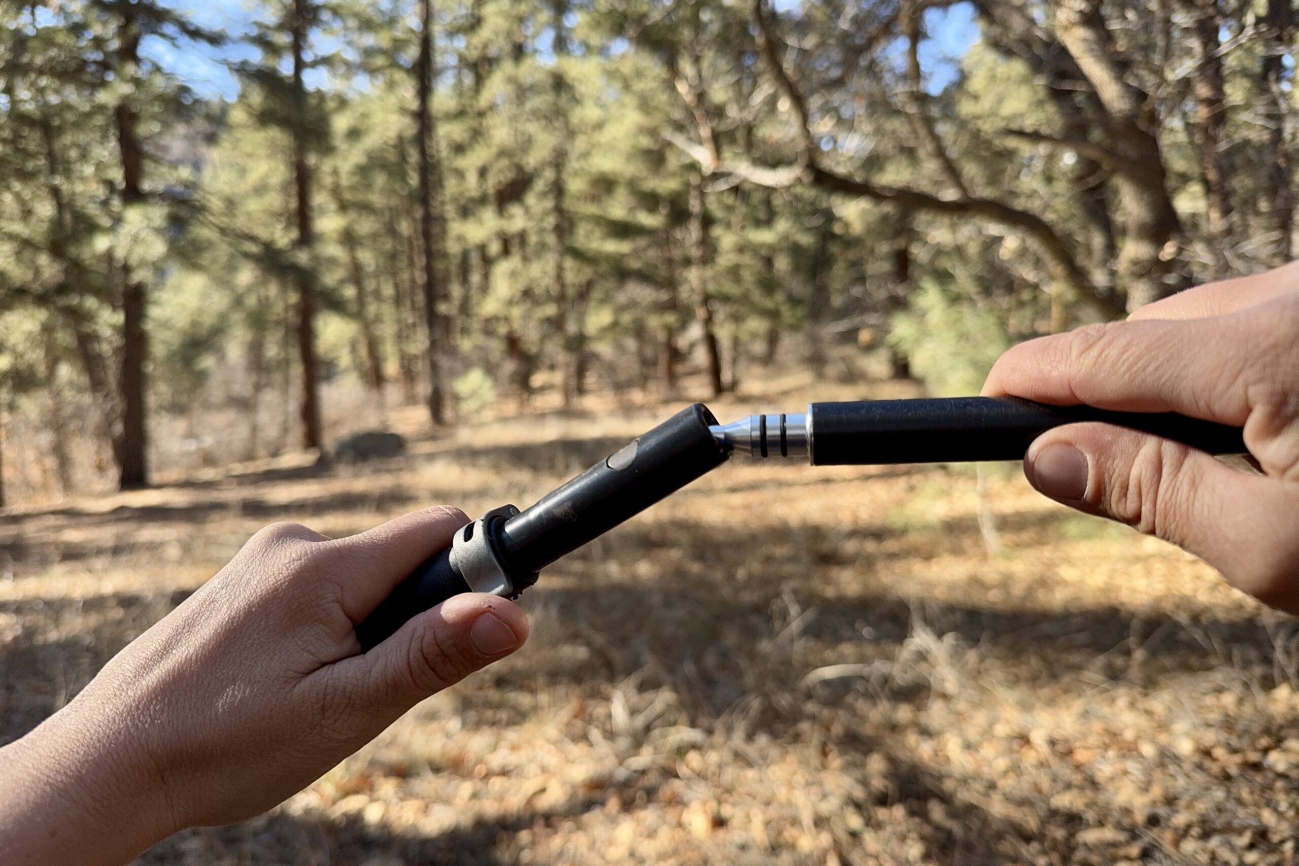 A close up of two hands folding joint on the Durston Iceline trekking poles in a forest.