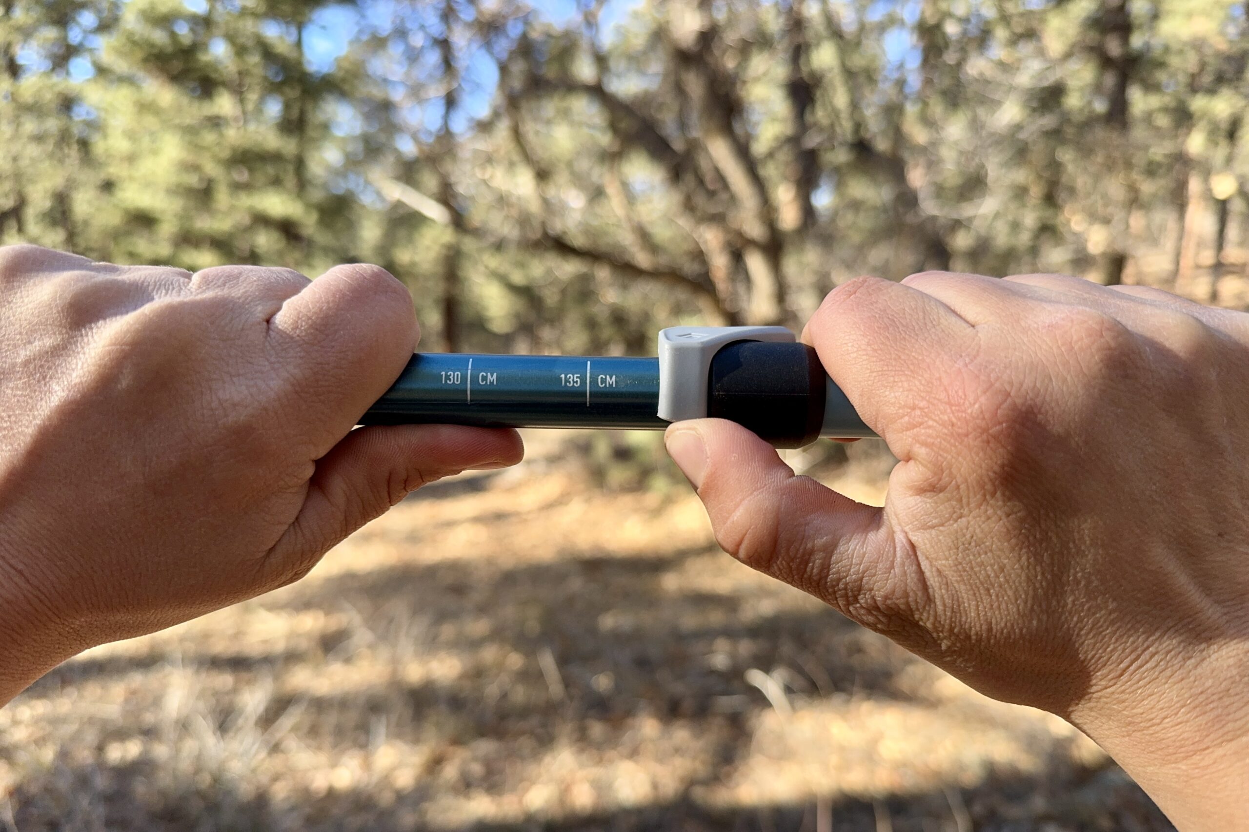 A close up of a hand closing a flick lock with trees in the background.