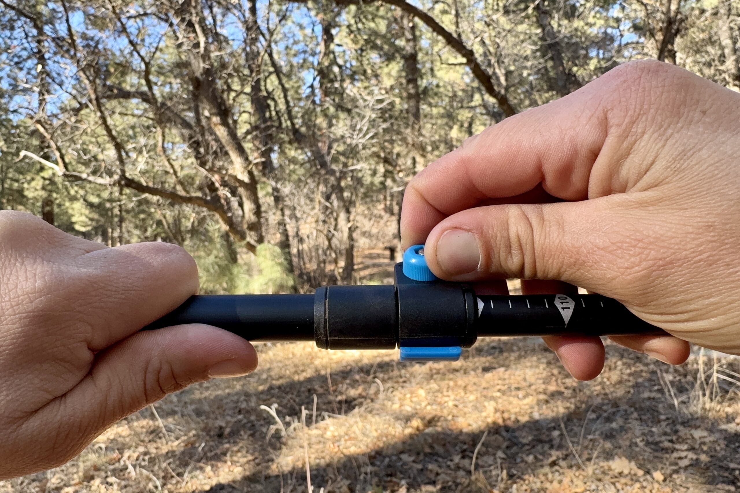 A close up of a hand twisting the flip lock tensioner on a trekking pole. A forest is in the background.