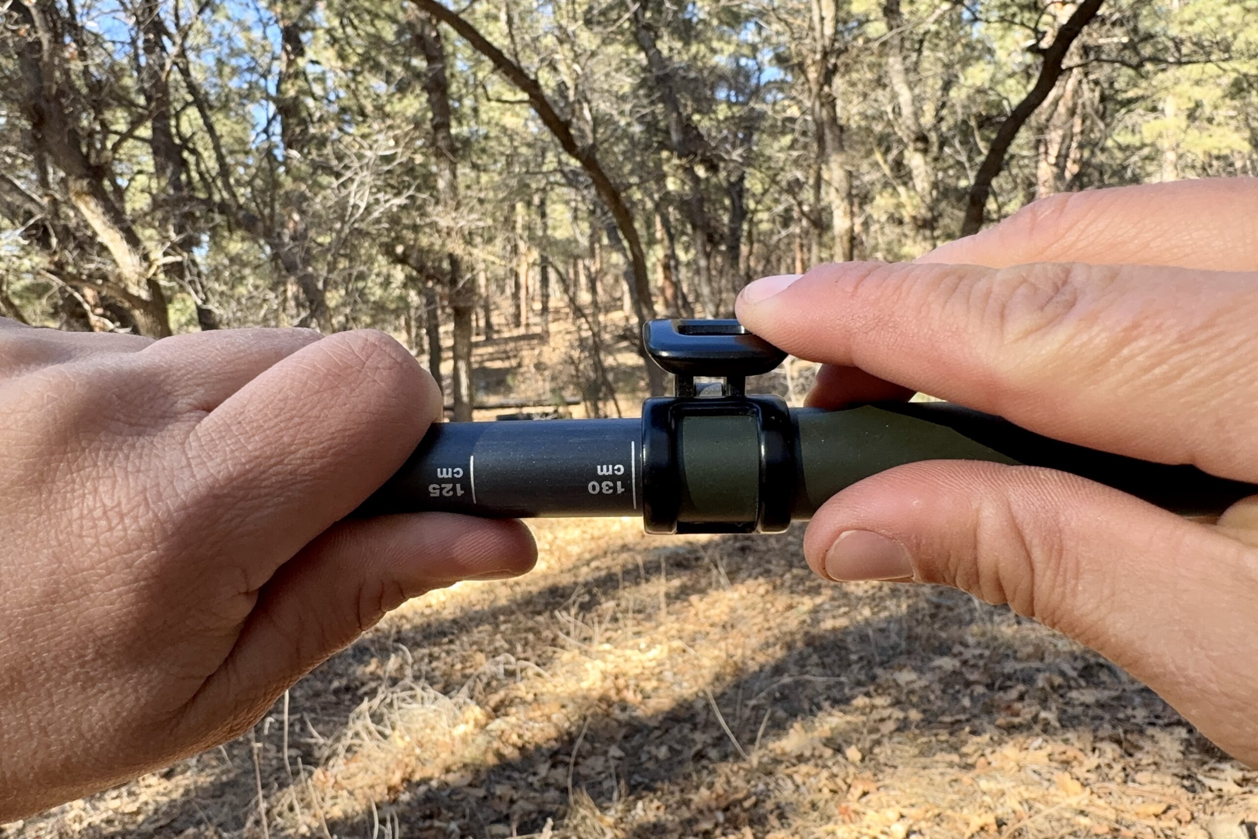 A close up of a hand closing a flick lock with trees in the background.