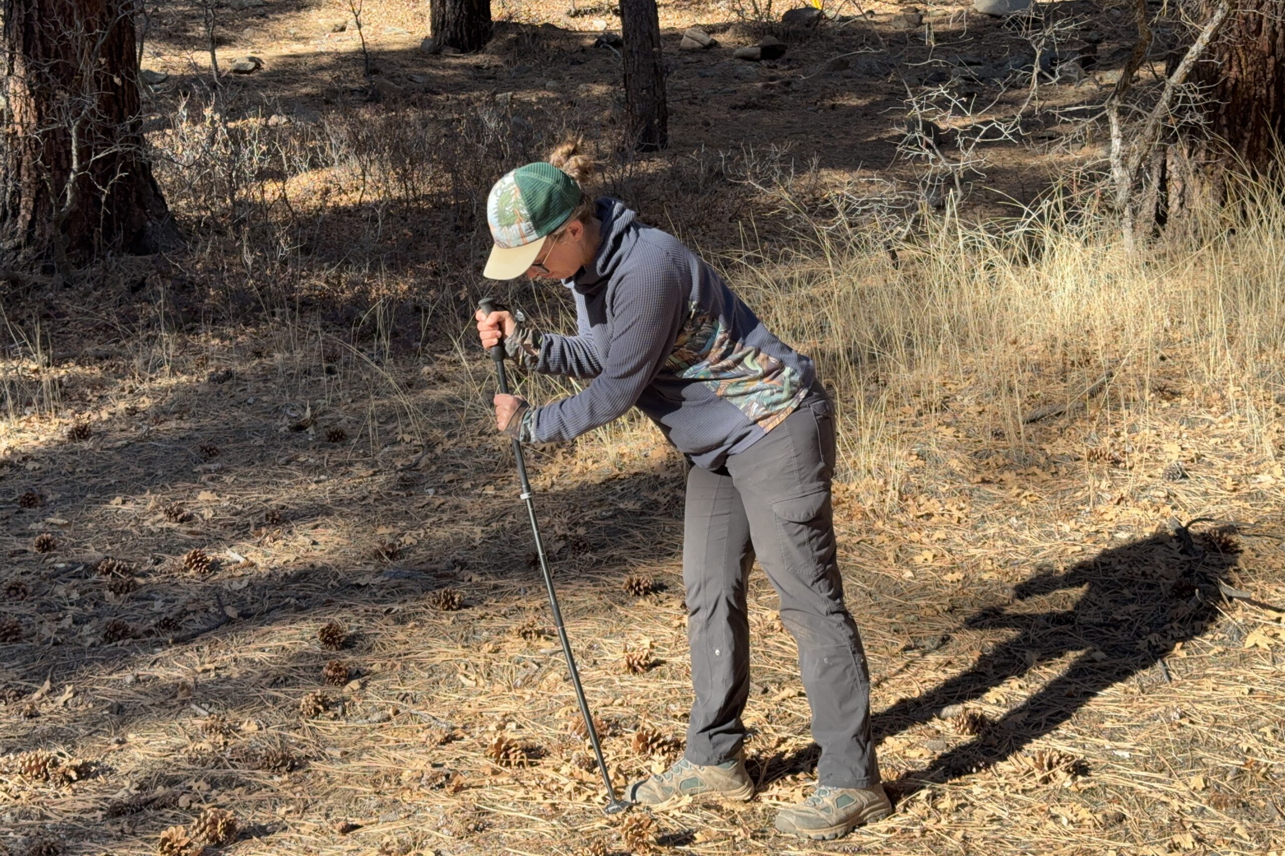 A close up of a person leaning on a trekking pole in the forest.