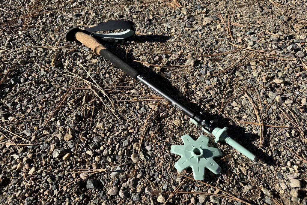 A collapsed trekking pole is laying on the ground with a winter basket sitting next to it.