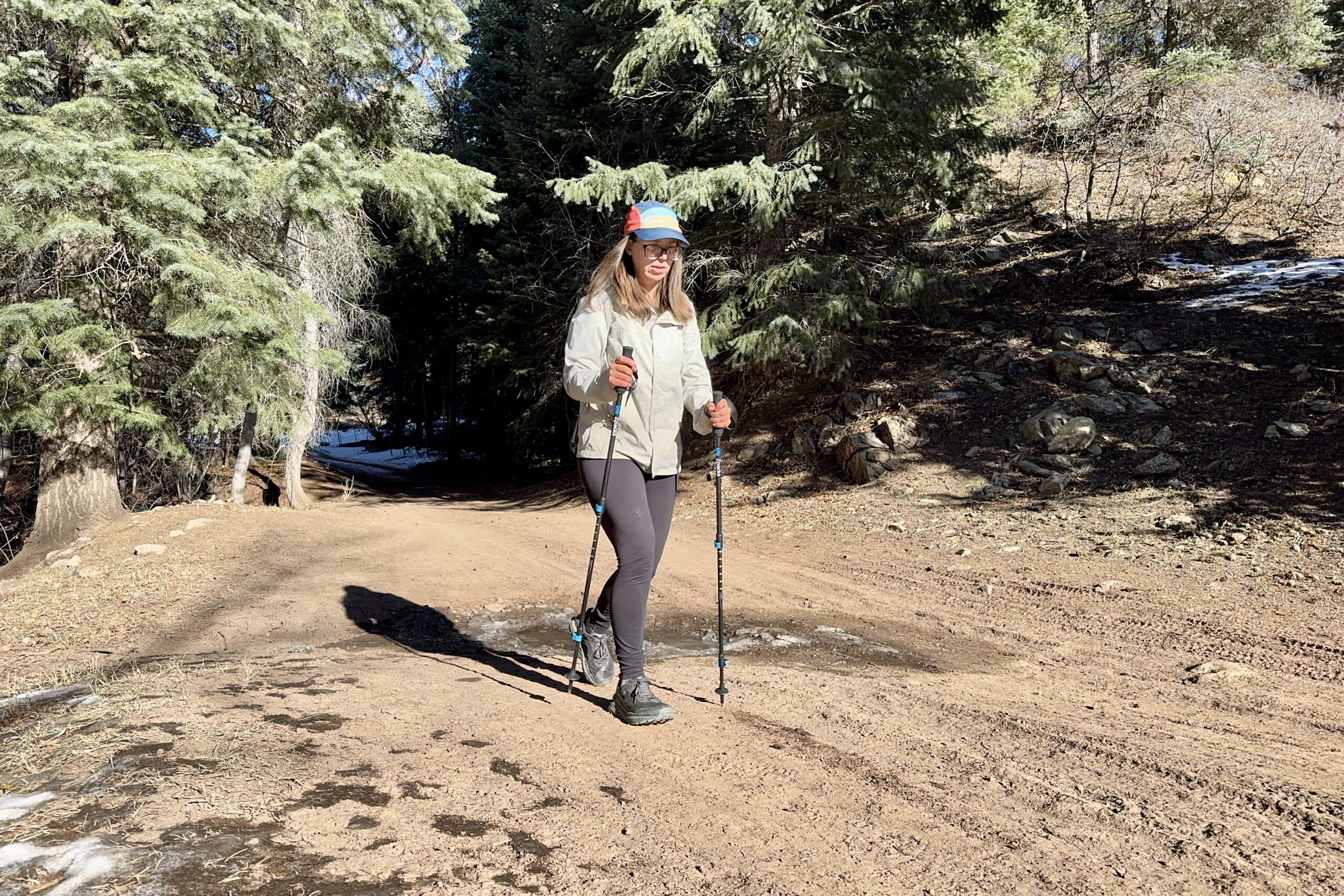 A person is walking down a dirt road while using a pair of trekking poles. The road is in a forest.