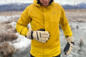 A man unzips his jacket while wearing gloves.