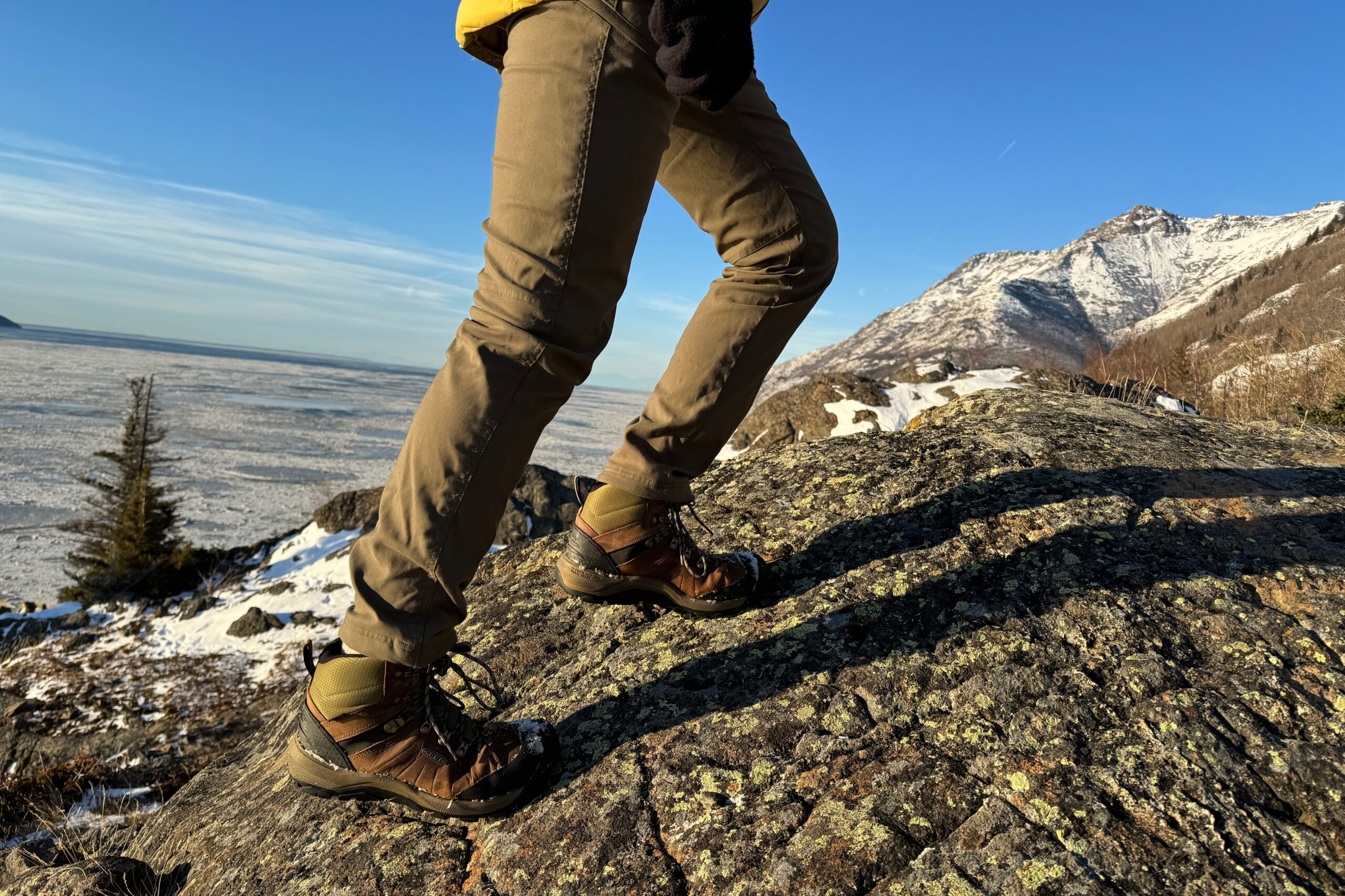A man walks up a rock with mountains in the background.