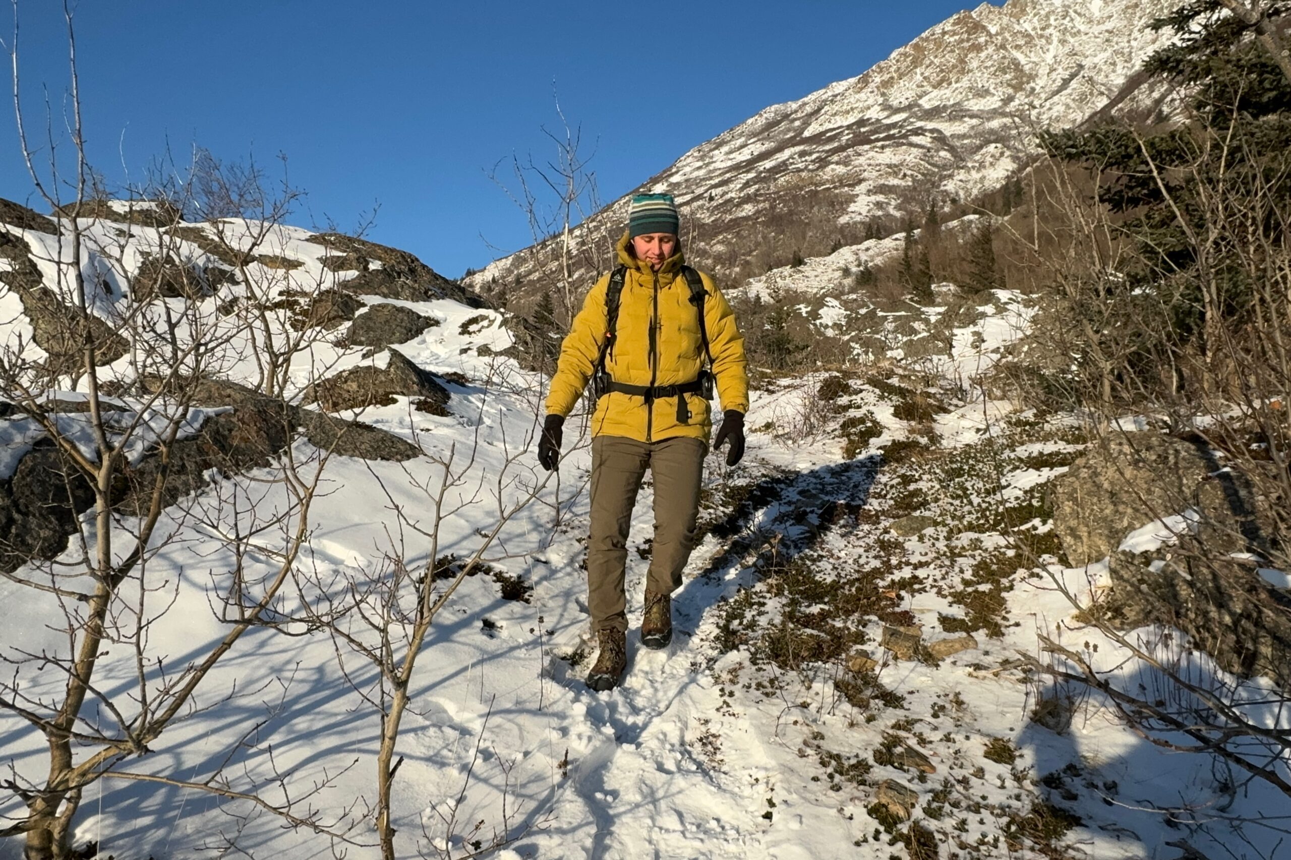A man walks down a snowy trail on a sunny day.