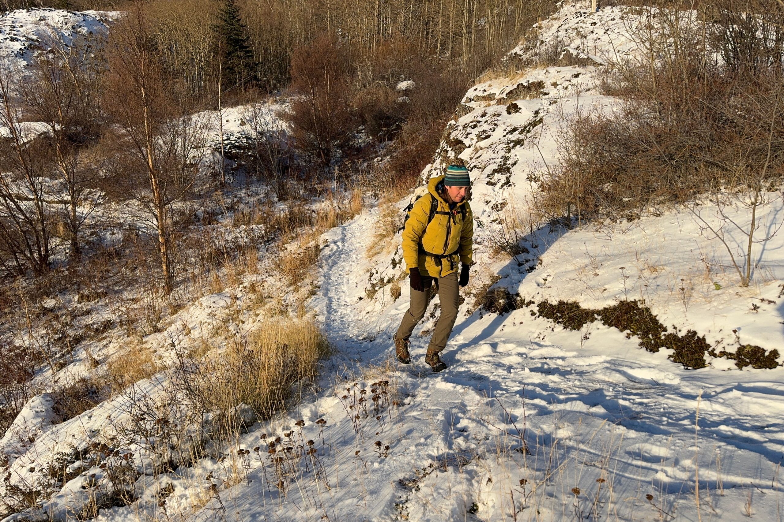 A man walks up a snowy trail wearing winter clothes.