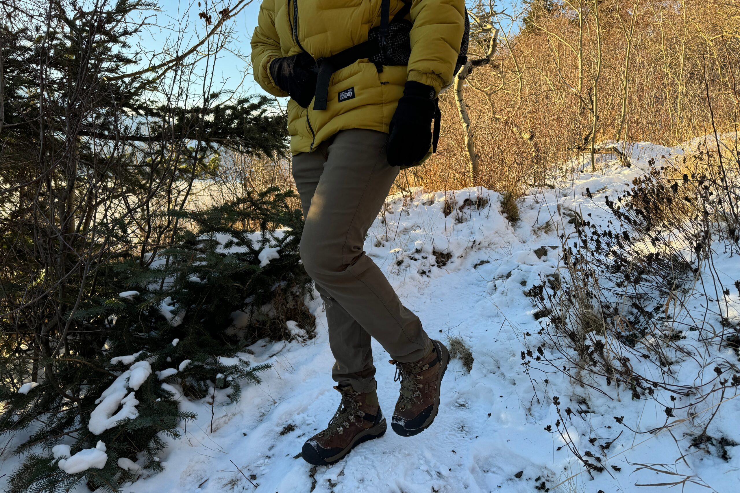 A man walks on a snowy hill in the shade of a tree.