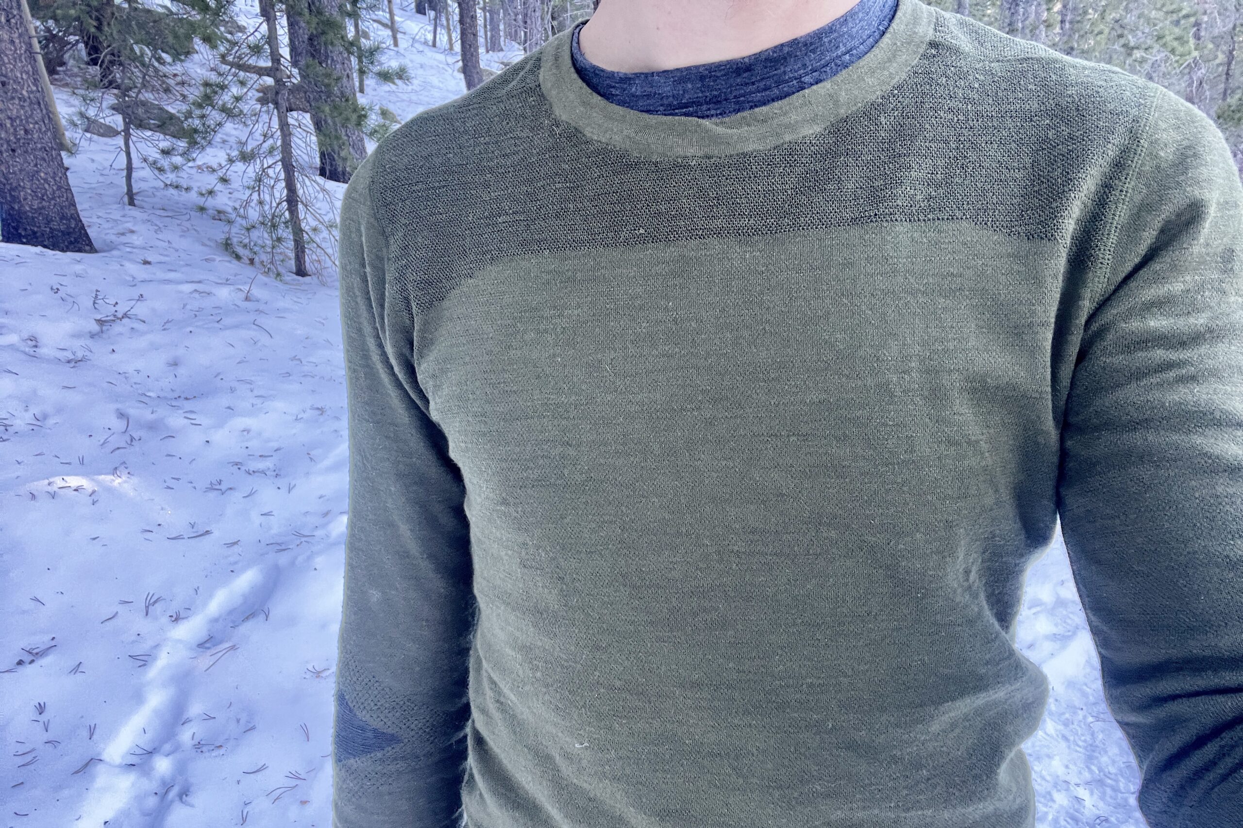 The top half of a man's torso with a snowy, woodsy background.