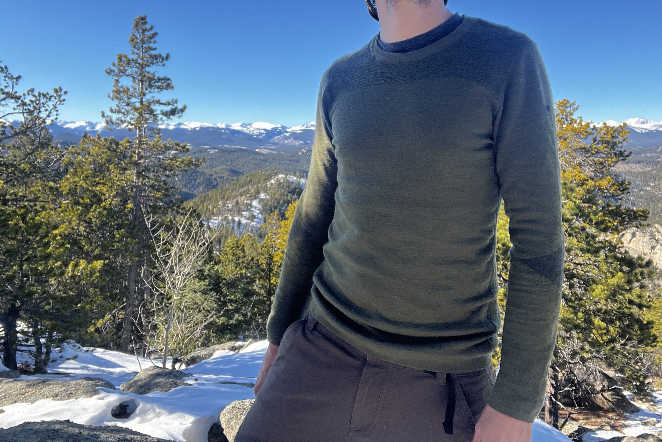 A hiker faces the camera while wearing the Smartwool Intraknit base layer. Mountains, sky, and trees in the background.