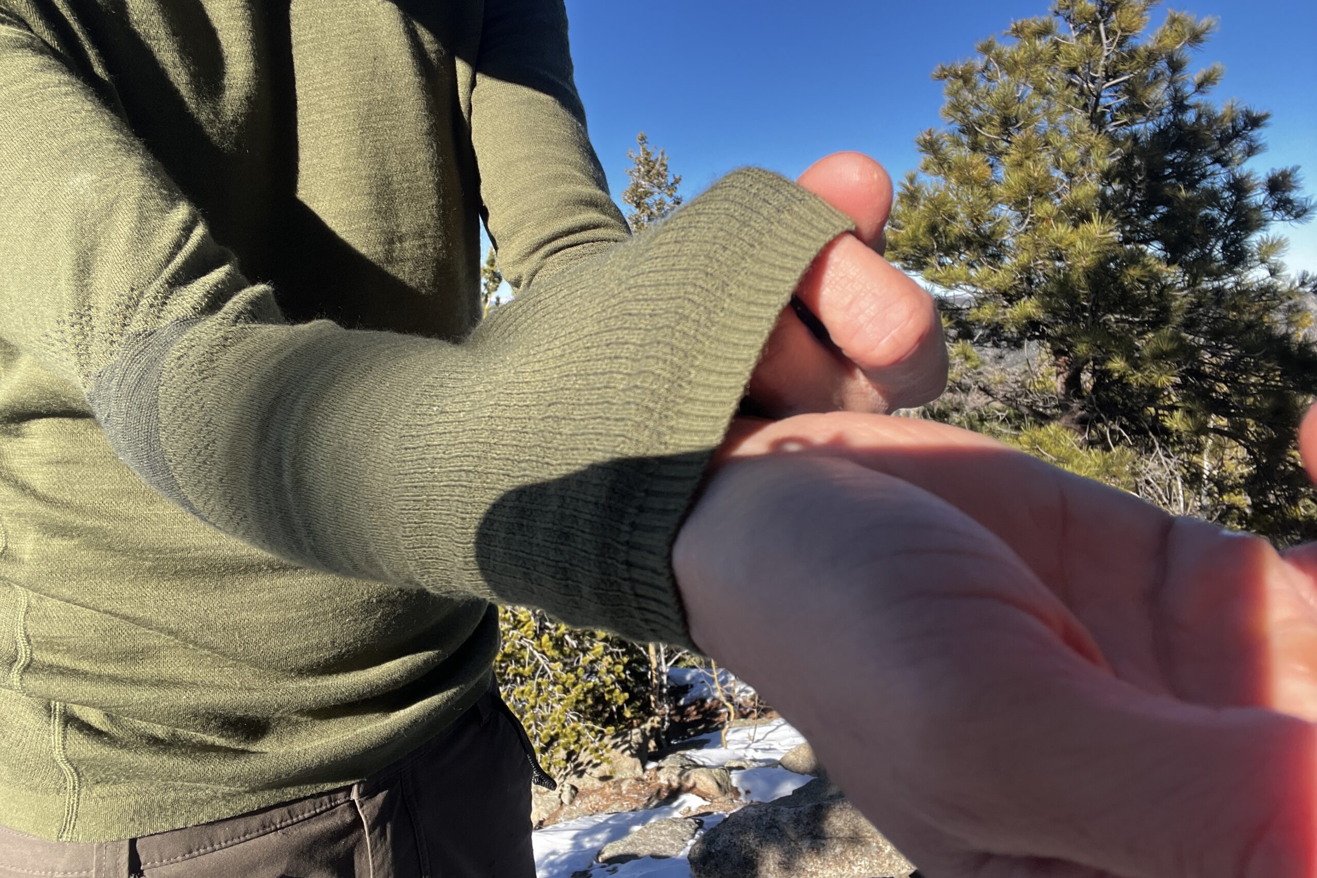 A hiker showing the wrist detail of the Smartwool Intraknit base layer. Trees and sky in the background.