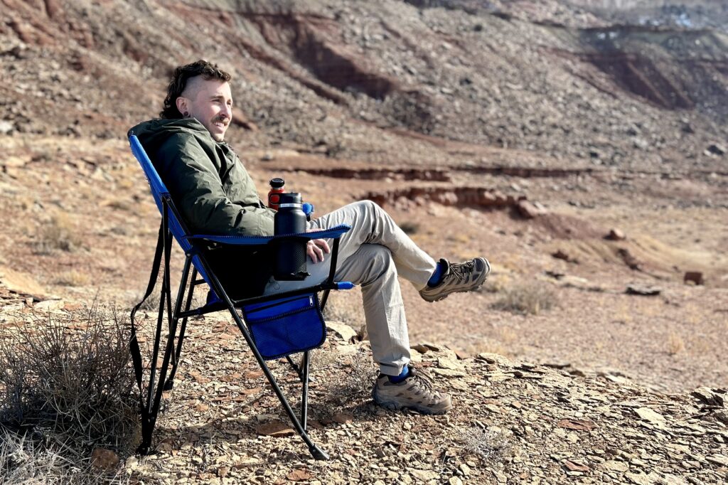 A man sits in a camping chair in a sunny desert setting.
