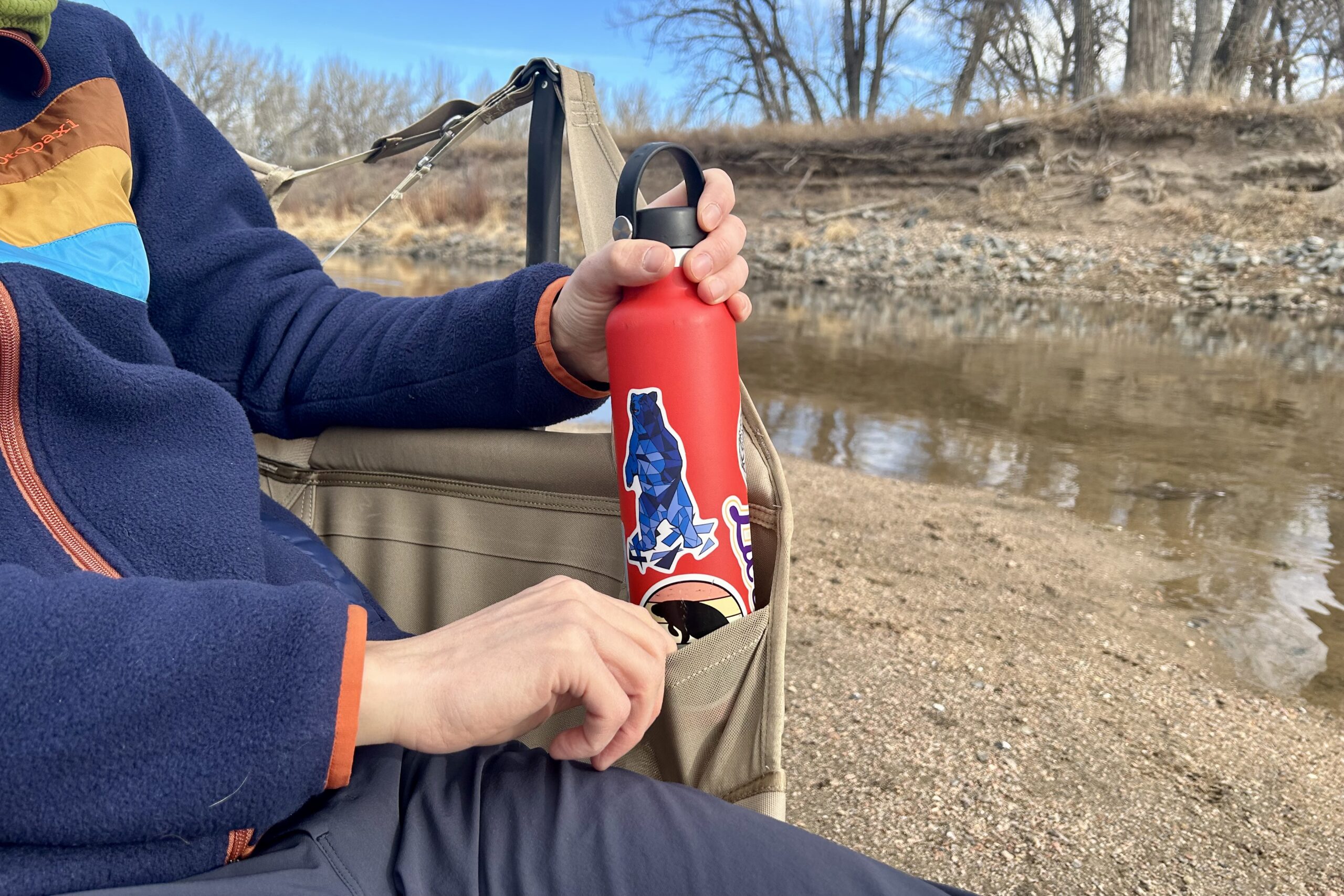 Close up of a camping chair cup holder with a person putting a bottle in it.