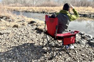 A man sits in a camping chair next to a river.