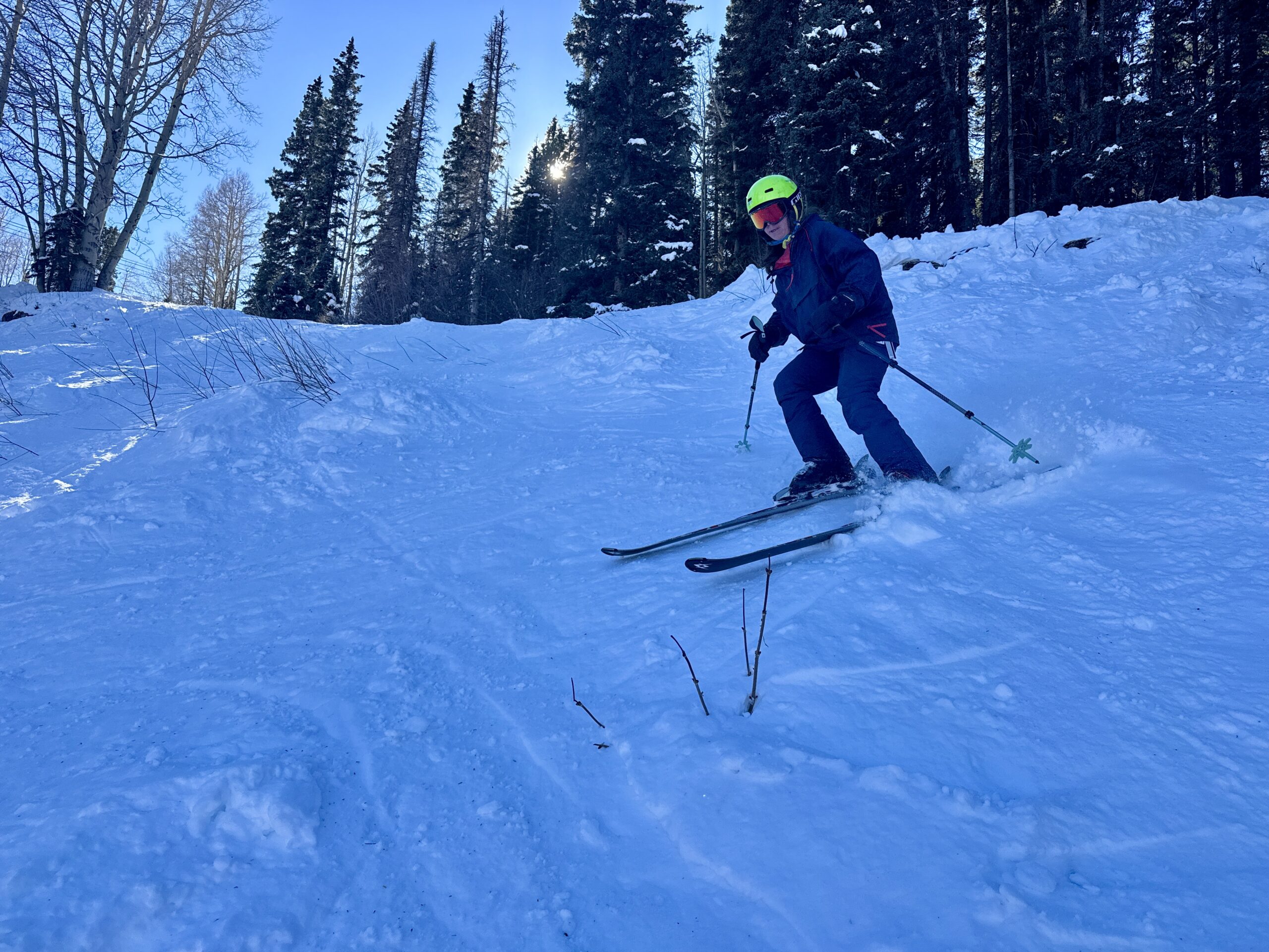 A person is skiing down a ski run in the trees holding the Black Diamond Pursuit trekking poles.