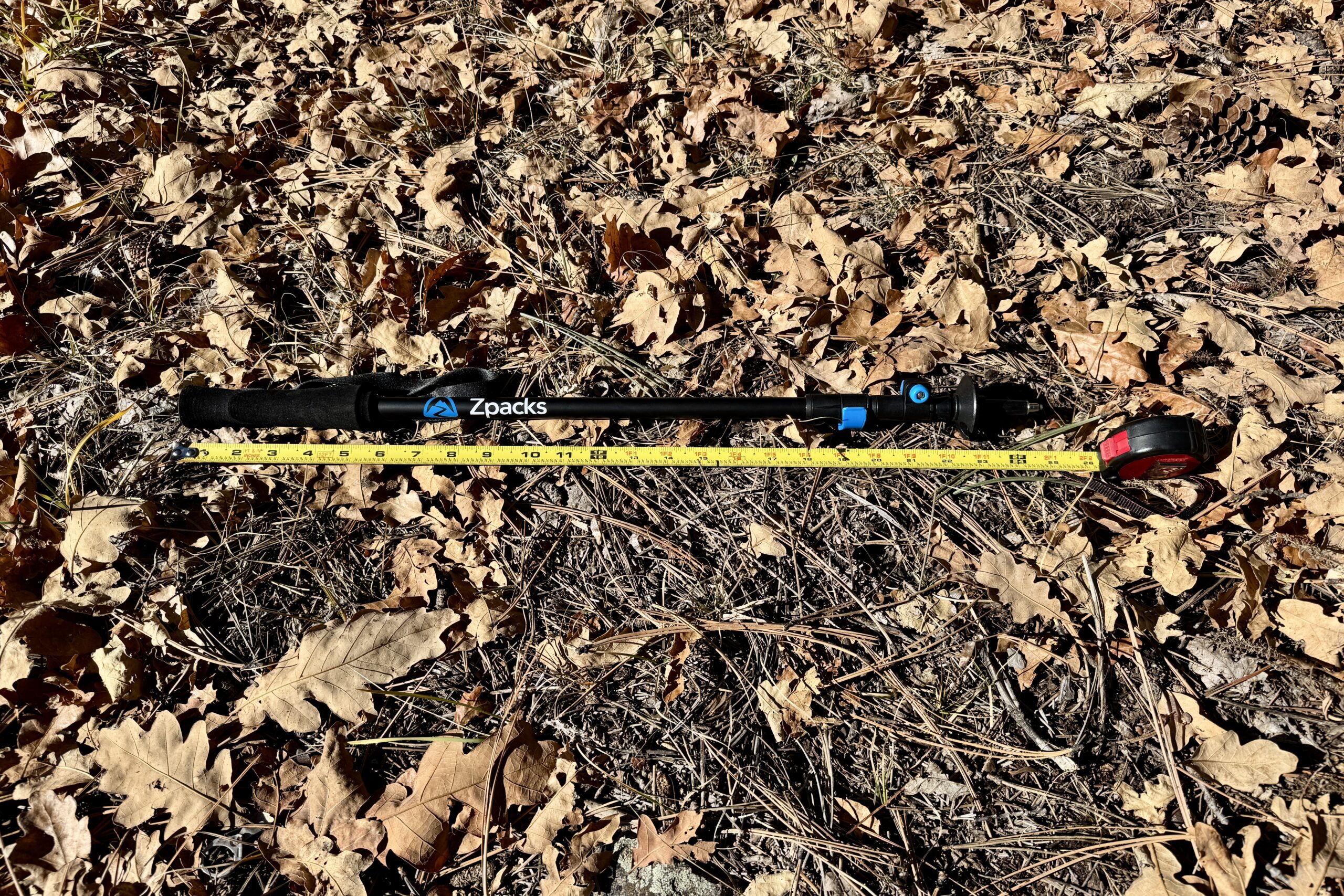 The Zpacks Minimalist pole is laying on the ground in some leaves with a measuring tape next to it.