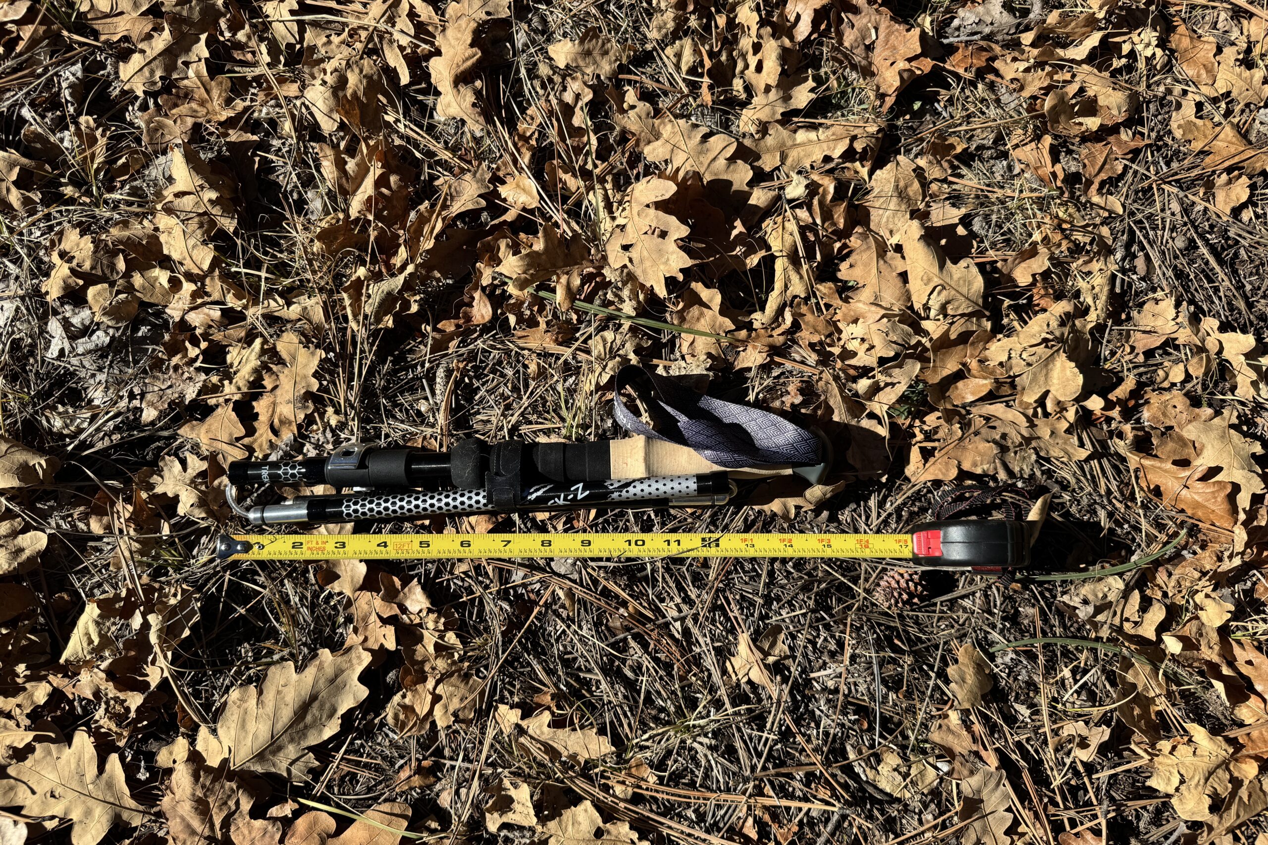 The Trekology Trek-Z 2.0 pole is laying on the ground in some leaves with a measuring tape next to it.