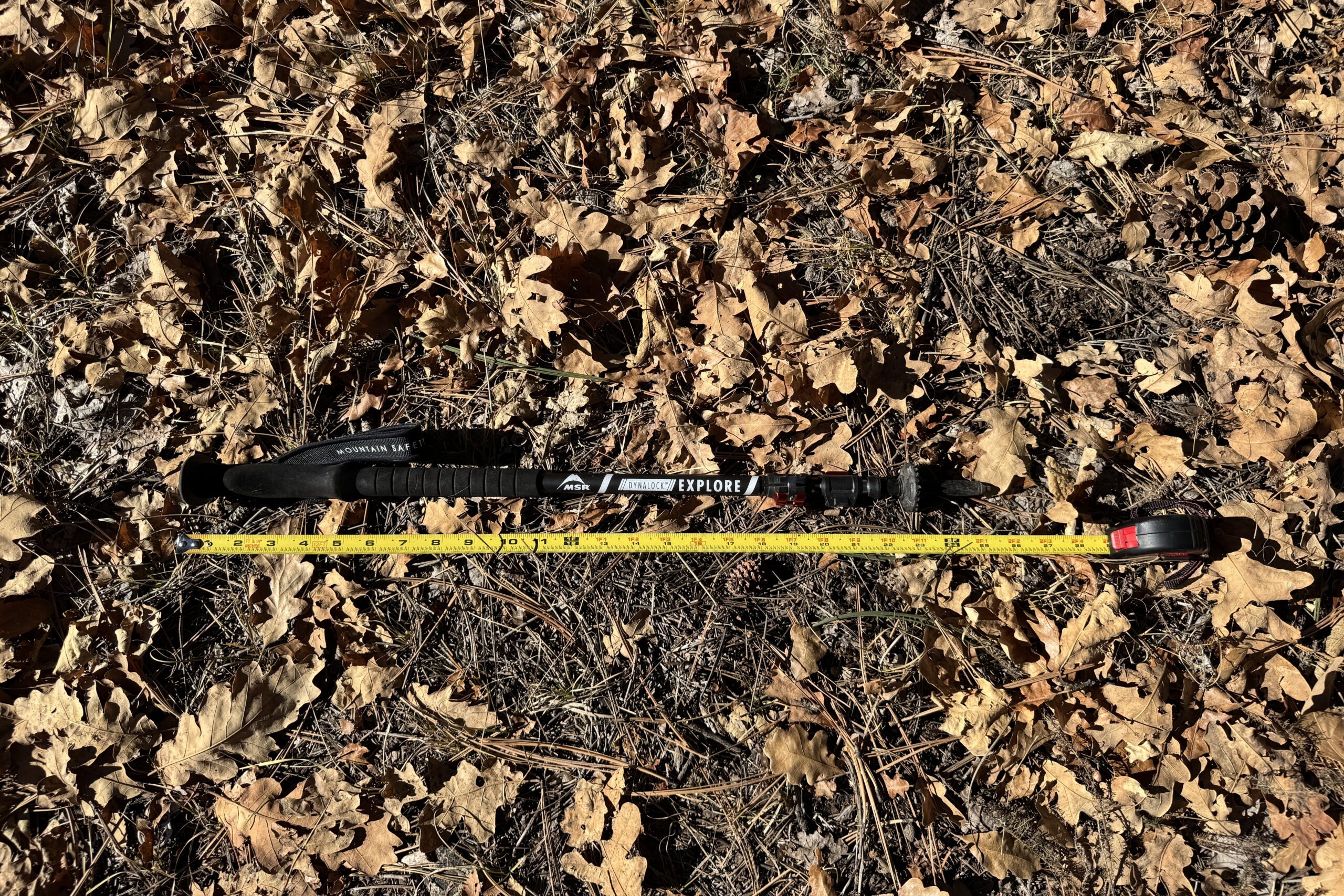 The MSR DynaLock Explore pole is laying on the ground in some leaves with a measuring tape next to it.