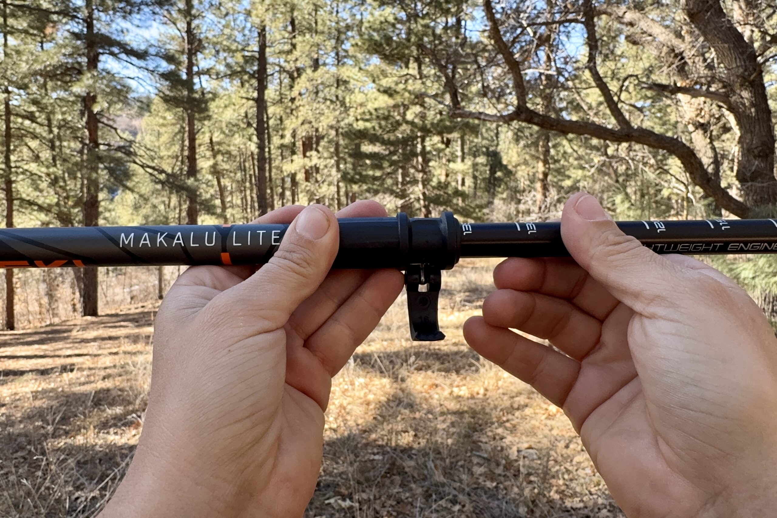 A close up of a hand closing a flick lock with trees in the background.